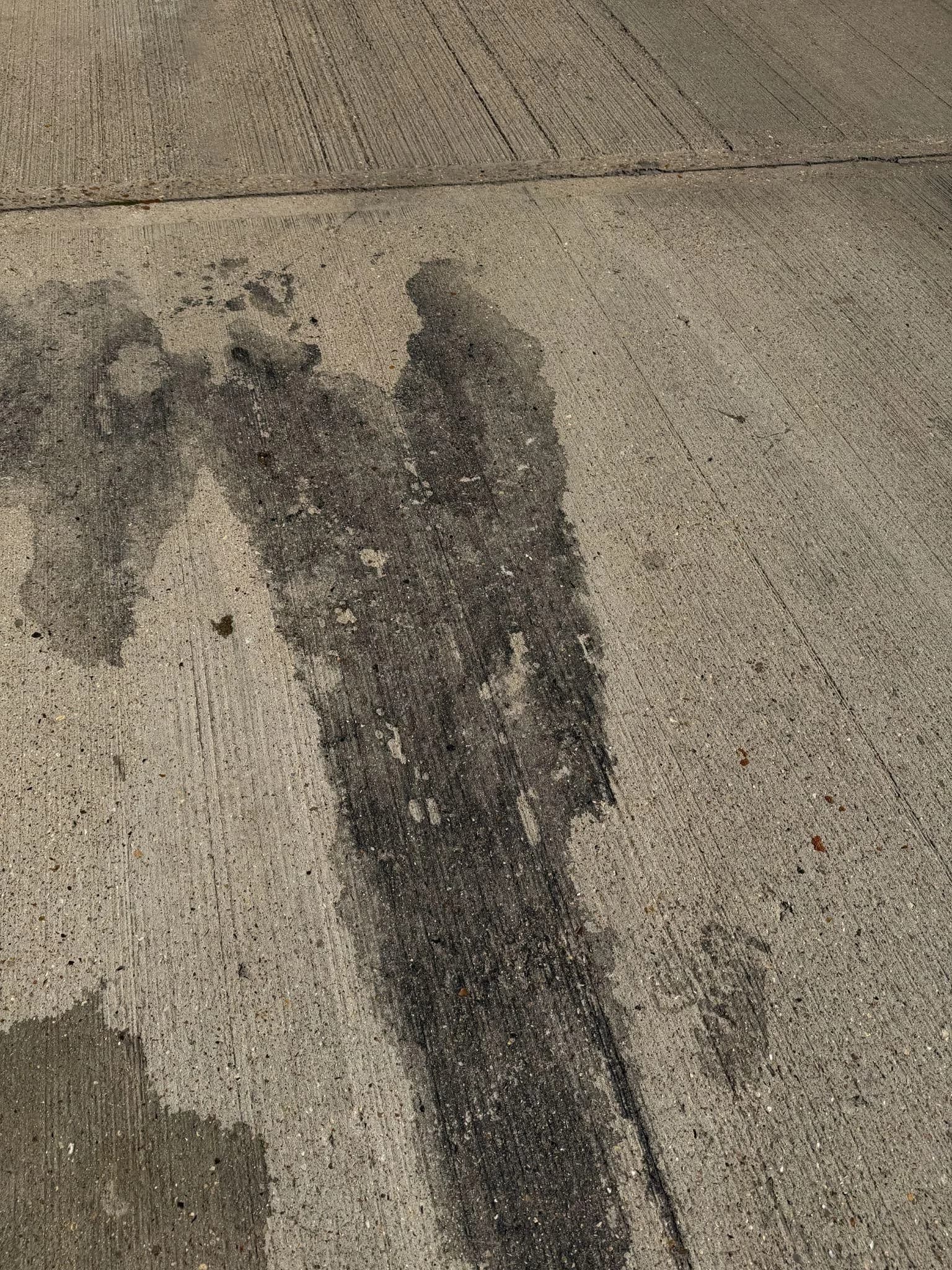 Close-up of dark oil staining and tyre marks across tamped concrete hardstanding beside an expansion joint