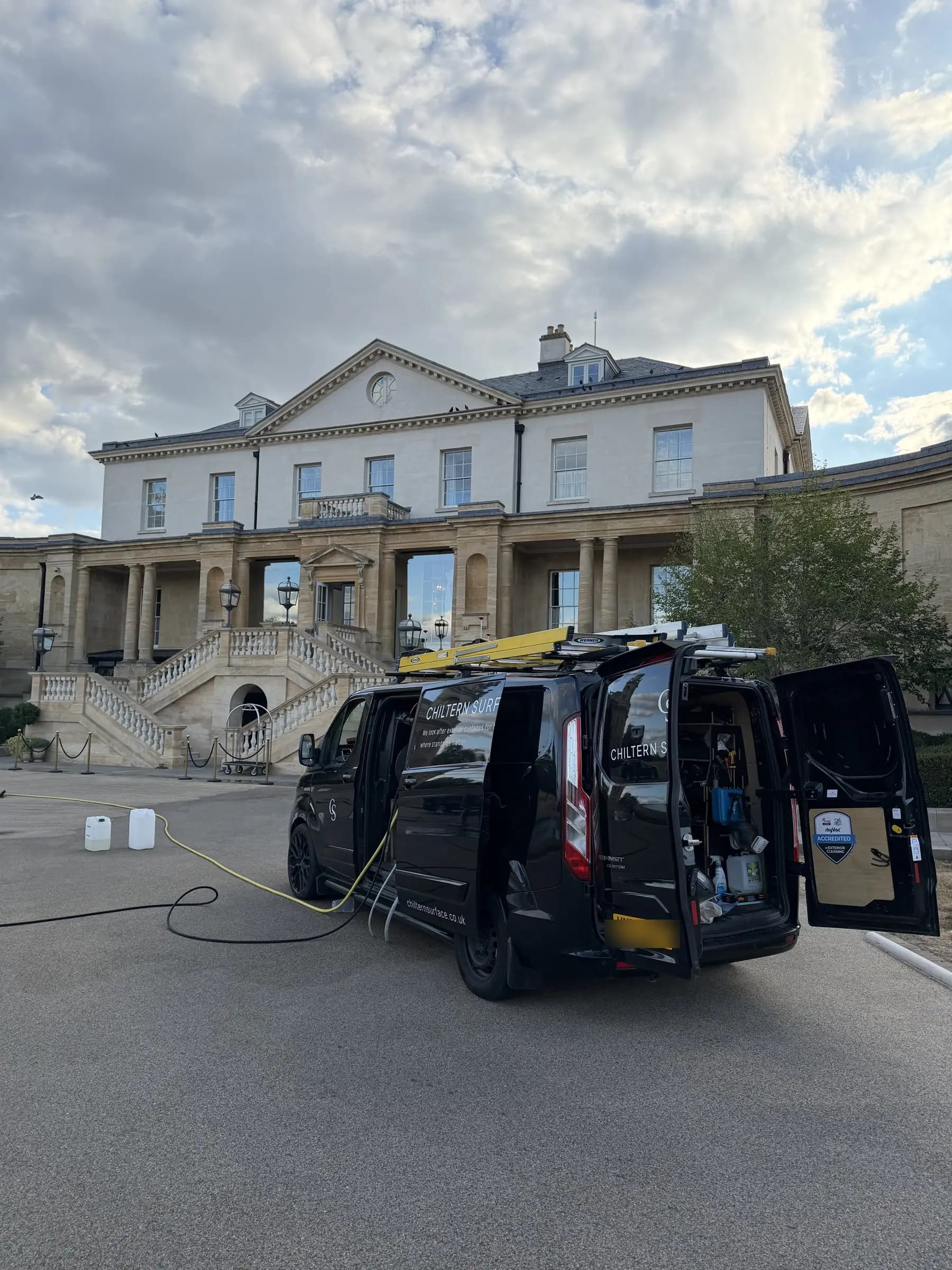 A Chiltern Surface Co van set up on the forecourt of a stone-fronted building, its rear doors open on racked equipment, with the hose run out across the surface