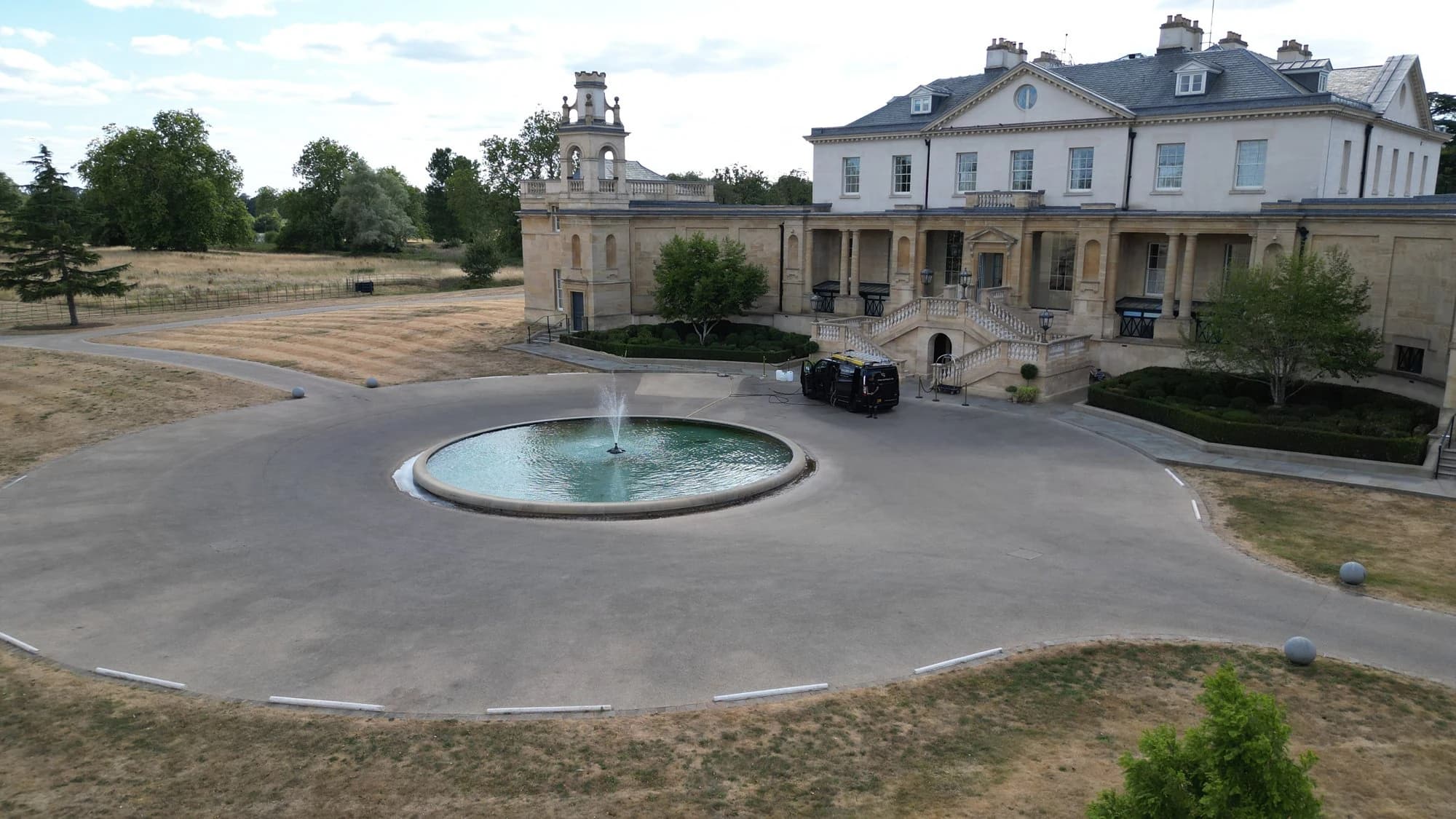Drone view of a stone-fronted building's forecourt and turning circle before cleaning, the surface darkened and patchy