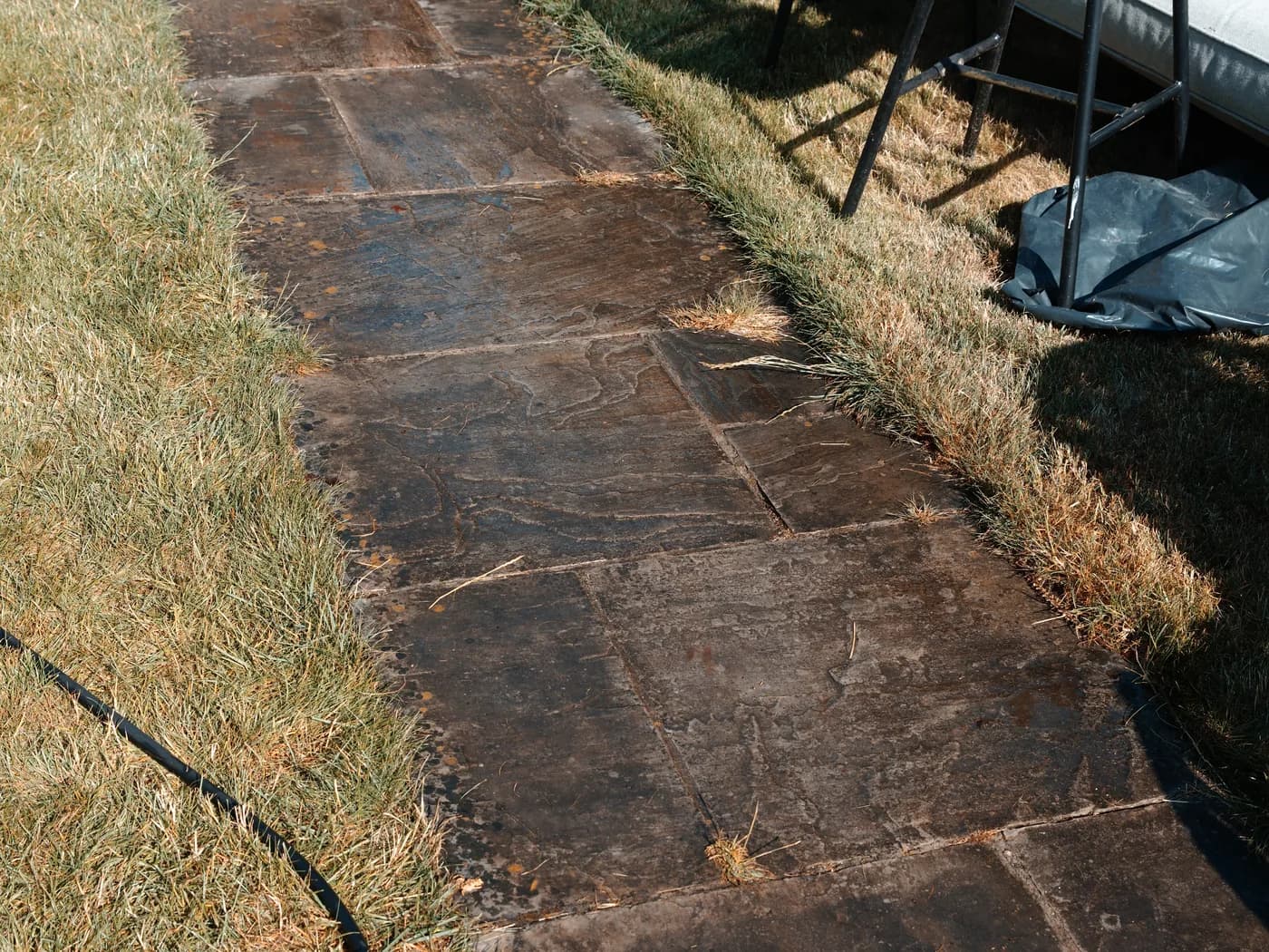 The sandstone patio cleared for work, with the garden table and chairs standing on the lawn alongside and hoses and a treatment container staged on the paving