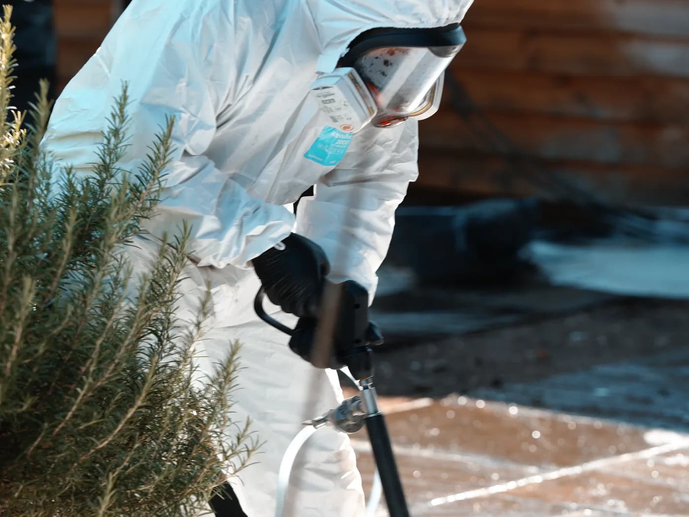A technician in protective coveralls and respirator bent low over the paving, directing treatment onto a localised area of the sandstone