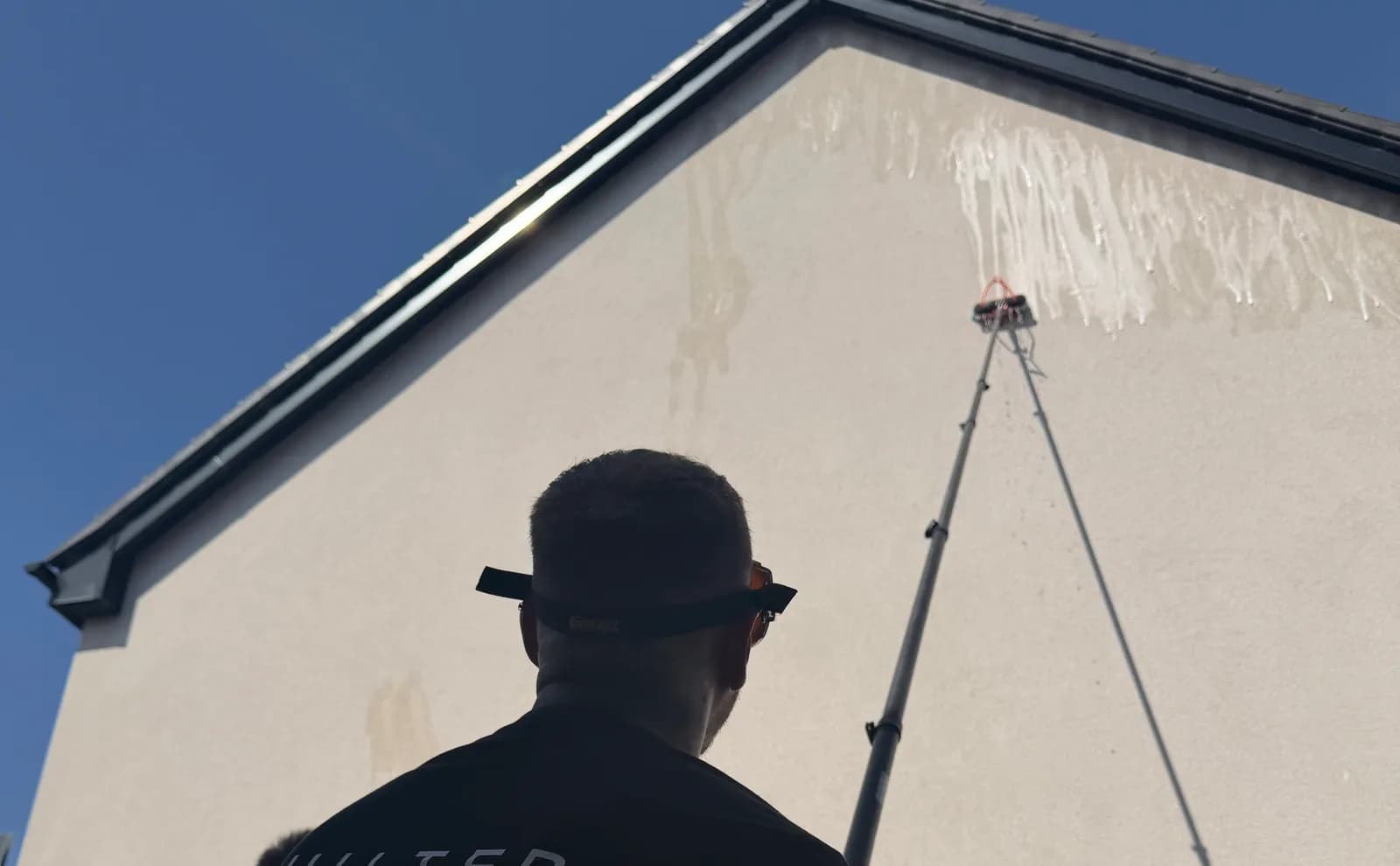 Chiltern Surface Co operative soft washing a rendered gable wall with a pole-fed brush, the low-pressure solution running down the render