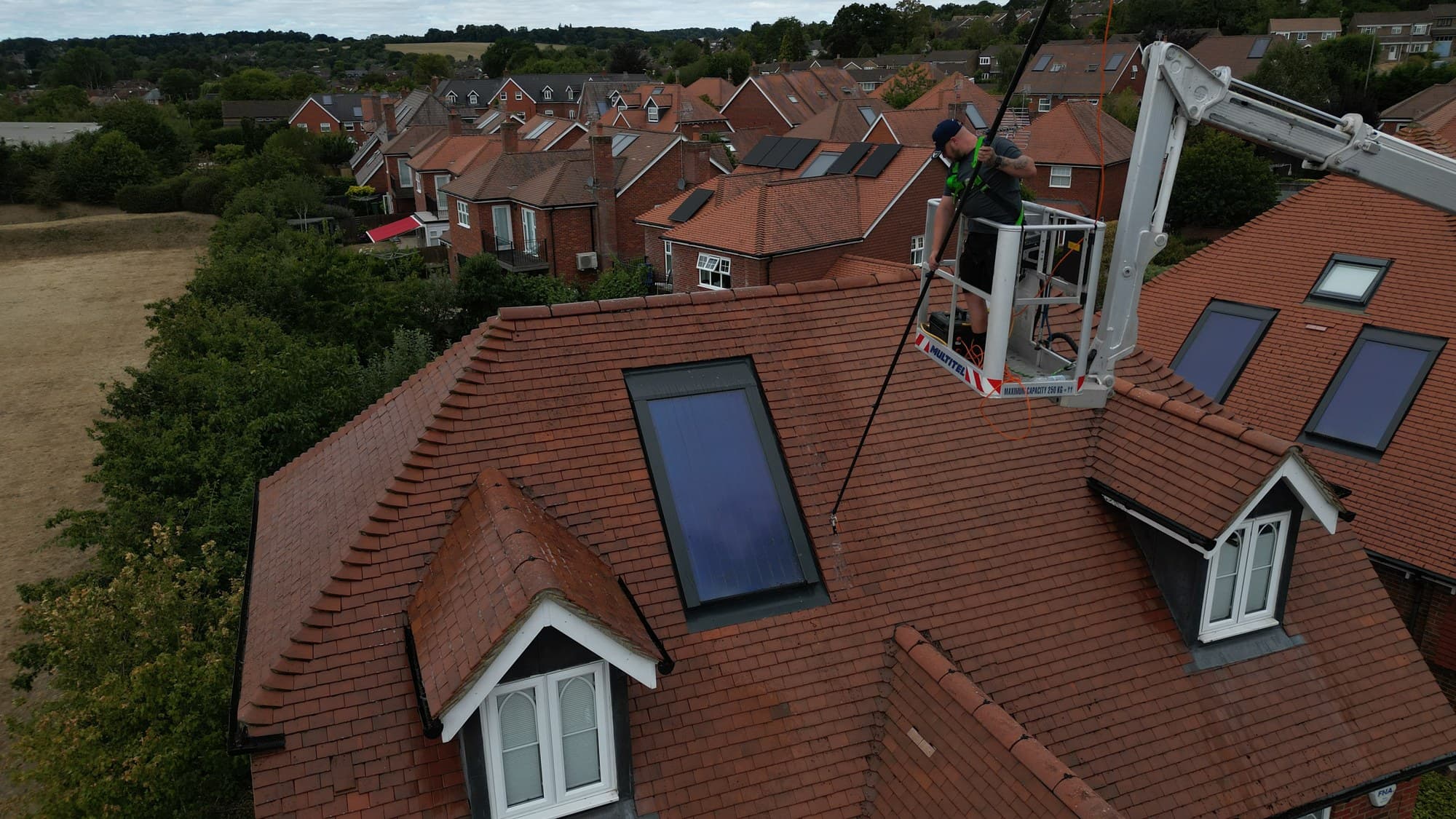 Aerial view of a tiled roof being cleaned by Chiltern Surface Co, the whole roof and property in frame