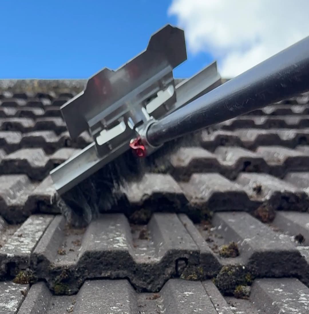 Moss being removed from concrete roof tiles by hand with a scraper before any treatment is applied