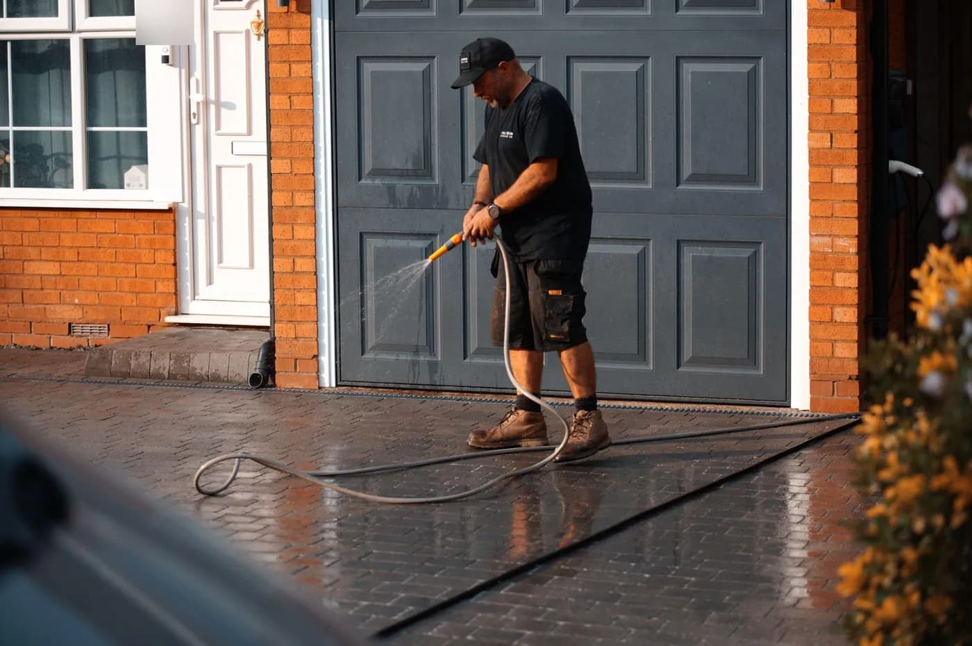 Operative rinsing dark block paving with a garden hose in front of a grey panelled garage door