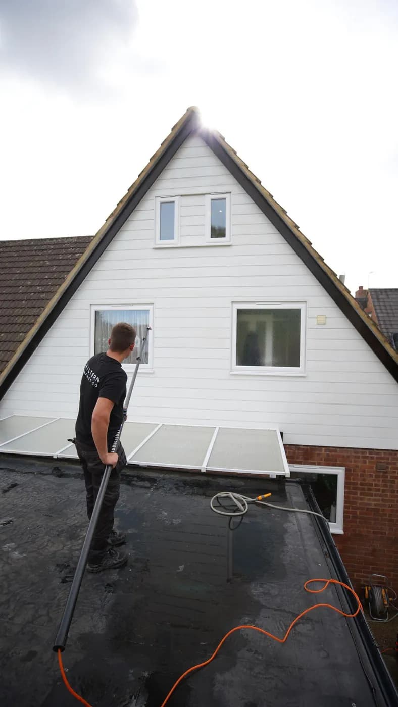 Operative on a flat roof rinsing around a window on a clean white clad gable with a water-fed pole
