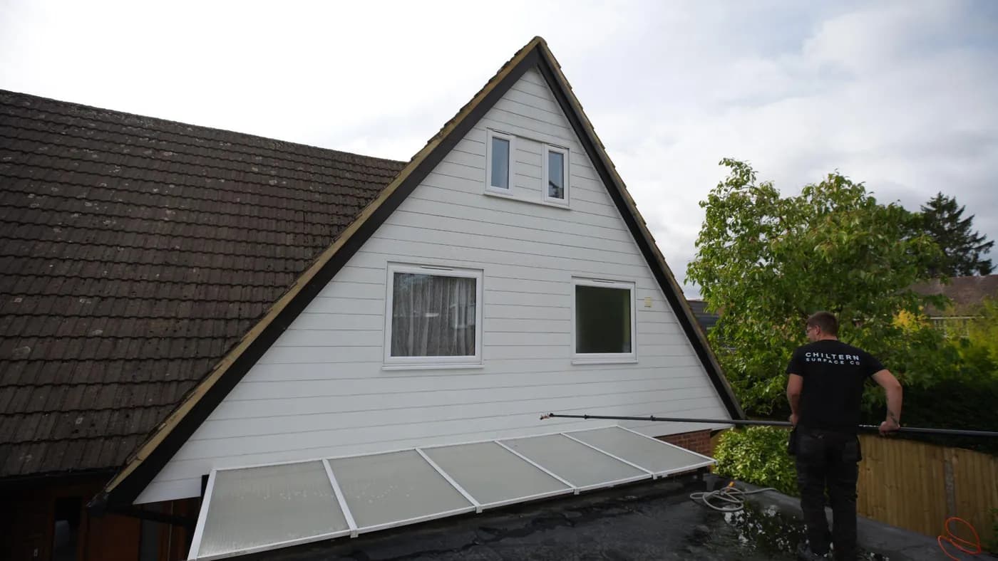 Clean white clad gable with an operative on a flat roof steering a water-fed pole along the base of the wall