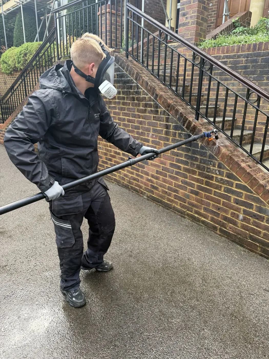 Technician applying a low-pressure soft wash treatment to brickwork