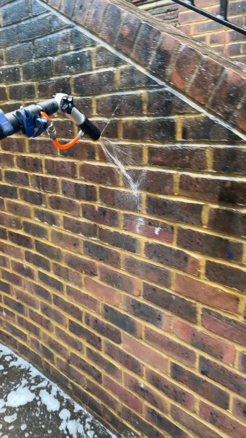 Close view of soft wash treatment sprayed onto brickwork at low pressure