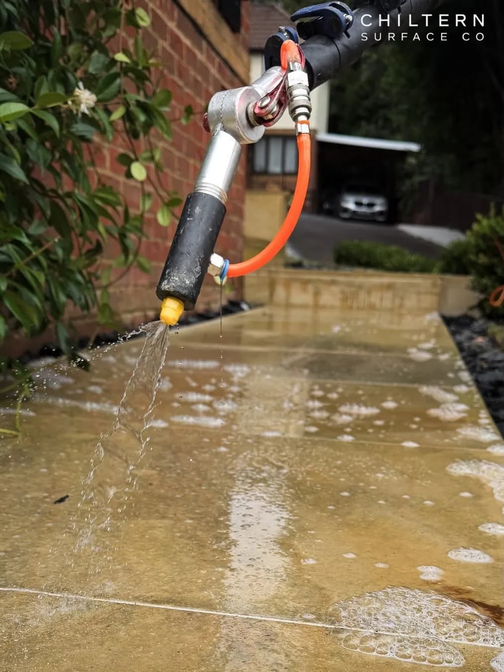 Close view of a lance nozzle releasing a gentle flow of treatment over wet buff sandstone slabs along a garden path