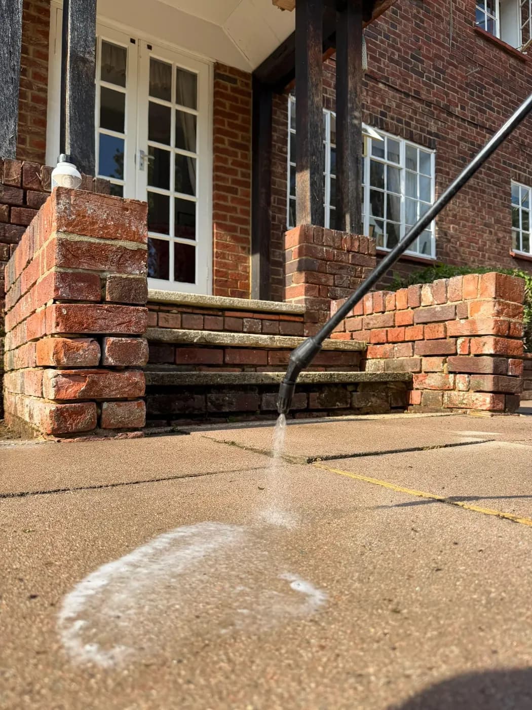 Lance applying a low-pressure treatment to textured paving slabs in front of brick steps with stone treads and French doors