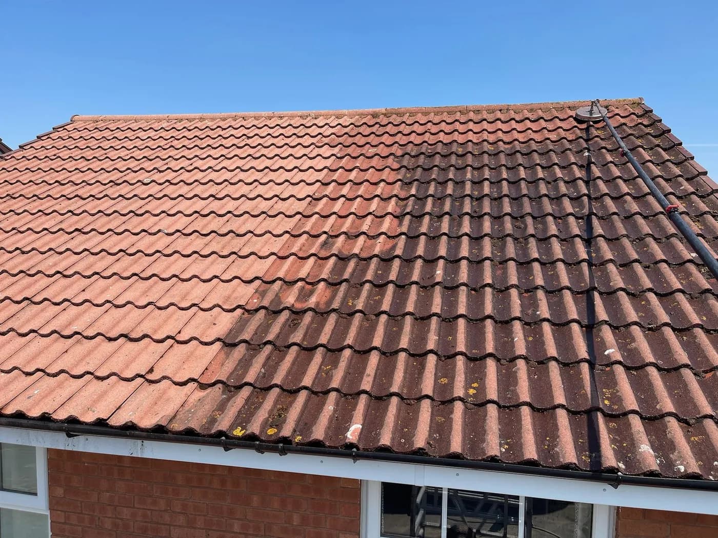 Concrete interlocking roof tiles half cleaned, with lichen-spotted tiles on one side and a rotary cleaner on a pole
