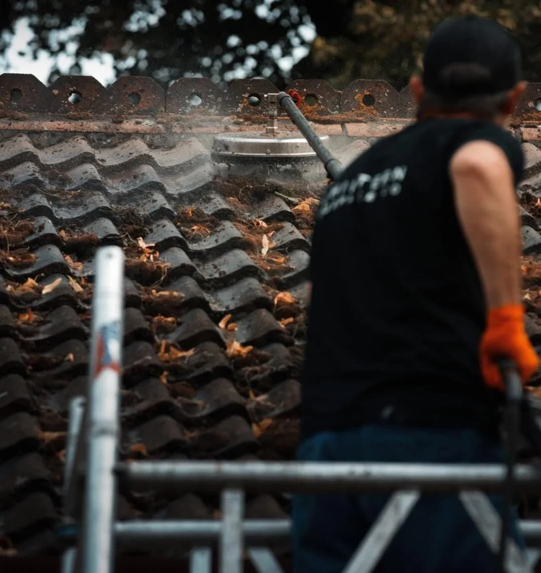 Operative on a tower guiding a rotary cleaner over deep-profiled tiles carpeted in moss and fallen leaves below a ridge
