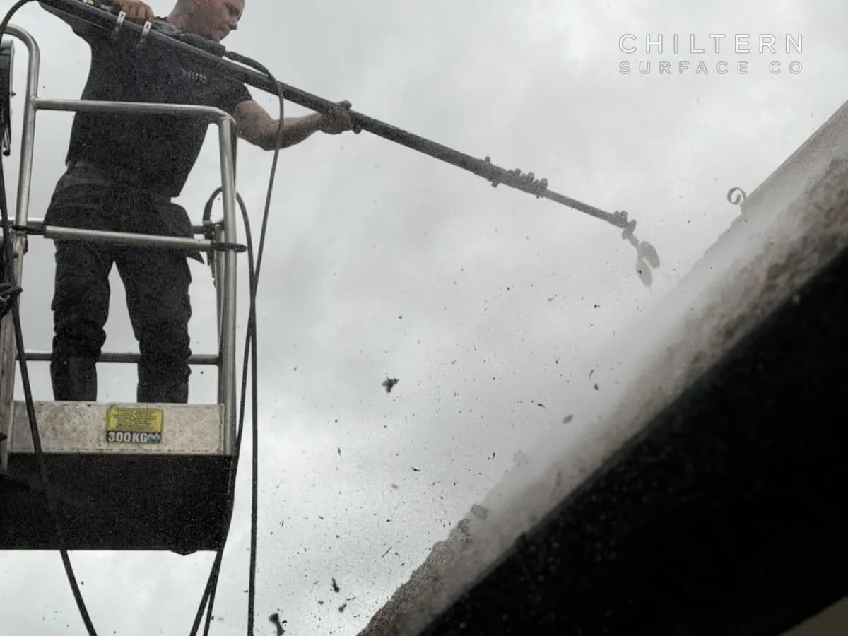 Operative in a mobile platform basket rinsing a tiled roof edge with a long lance as loosened moss falls away