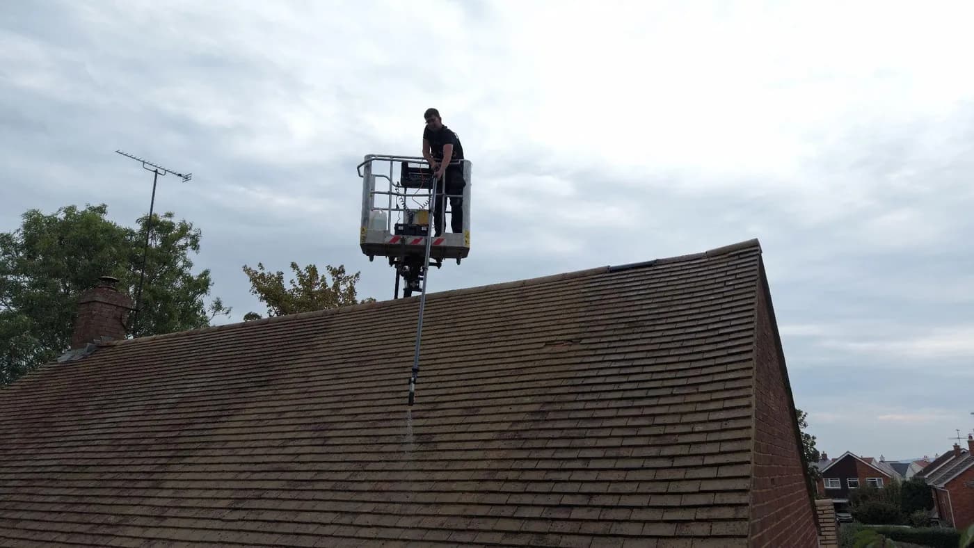 Operative in a lift basket above a plain-tile roof, applying a gentle low-pressure spray from a pole lance