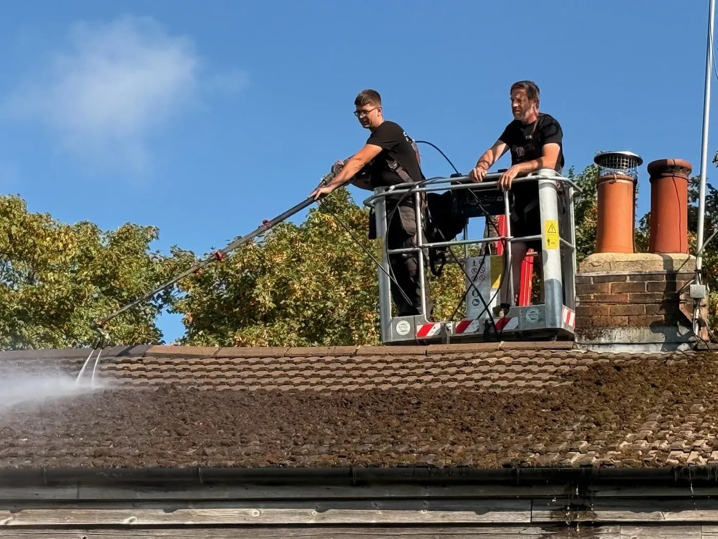 Low-pressure moss removal on a concrete tile roof, worked from a powered access platform