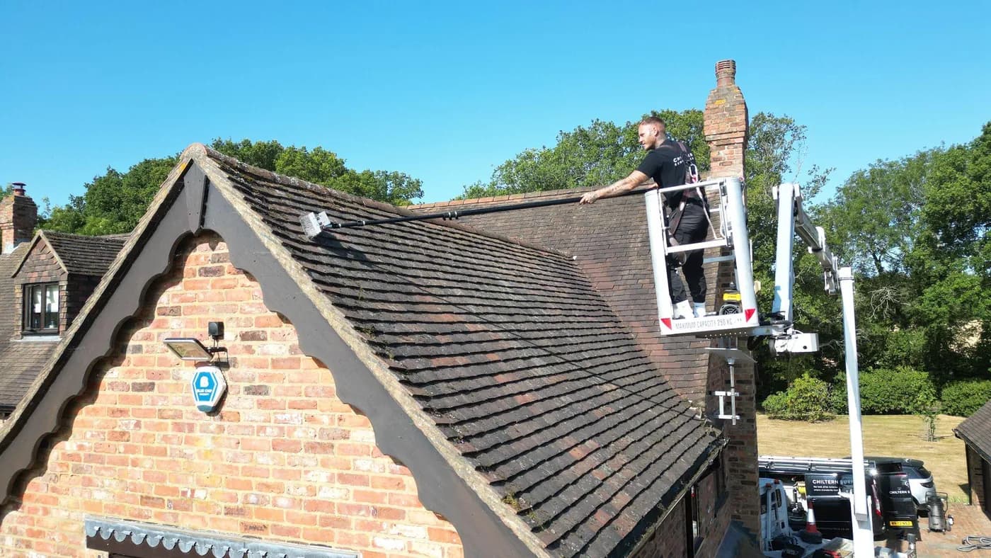 Operative on a raised platform brushing moss from an old clay plain-tile roof above a red-brick gable