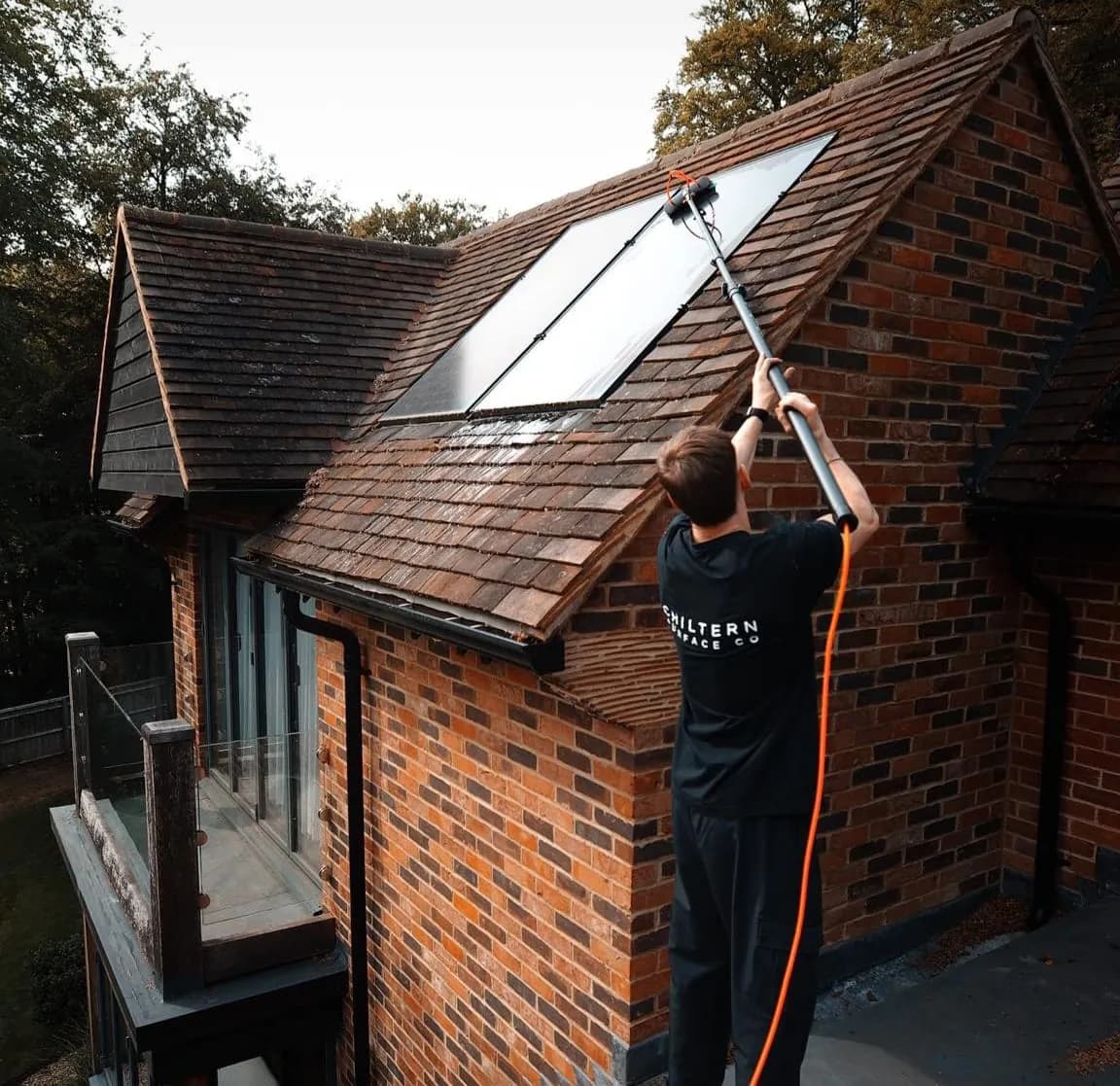 Operative on a flat roof using a water-fed pole and brush on two solar panels set in a clay-tiled roof