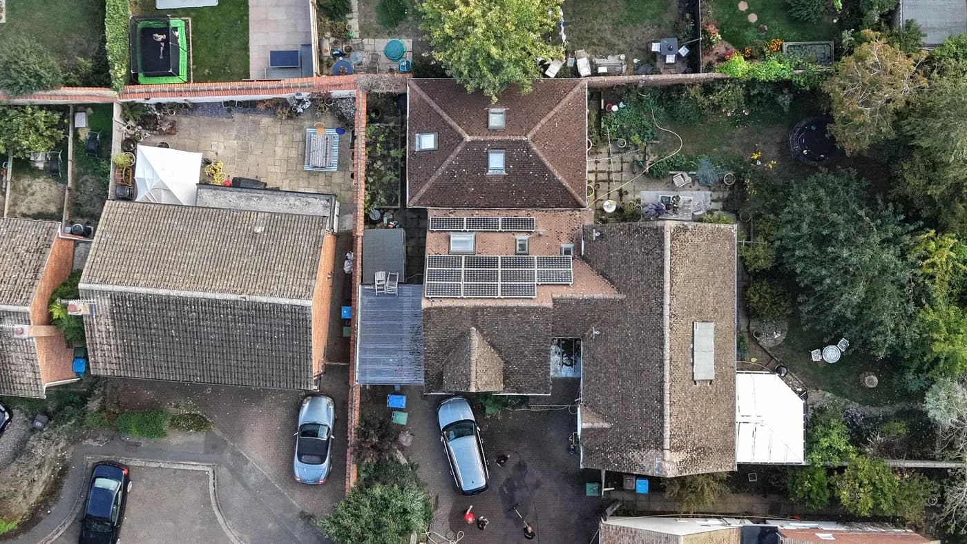 Overhead view of a detached house with two groups of solar panels on a rear roof slope, gardens and trees around it