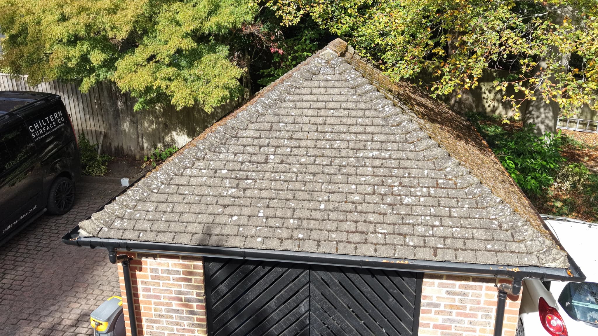 Aerial view of a hipped tile roof with moss and lichen across the slope, black gutters and a Chiltern Surface Co van parked alongside