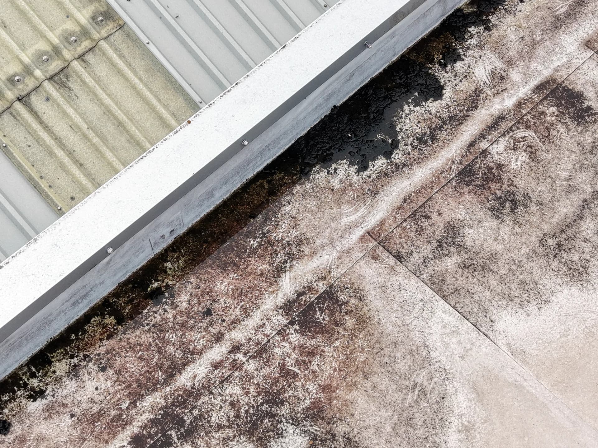 Aerial view of a parapet box gutter with a stained membrane beside a profiled-metal roof