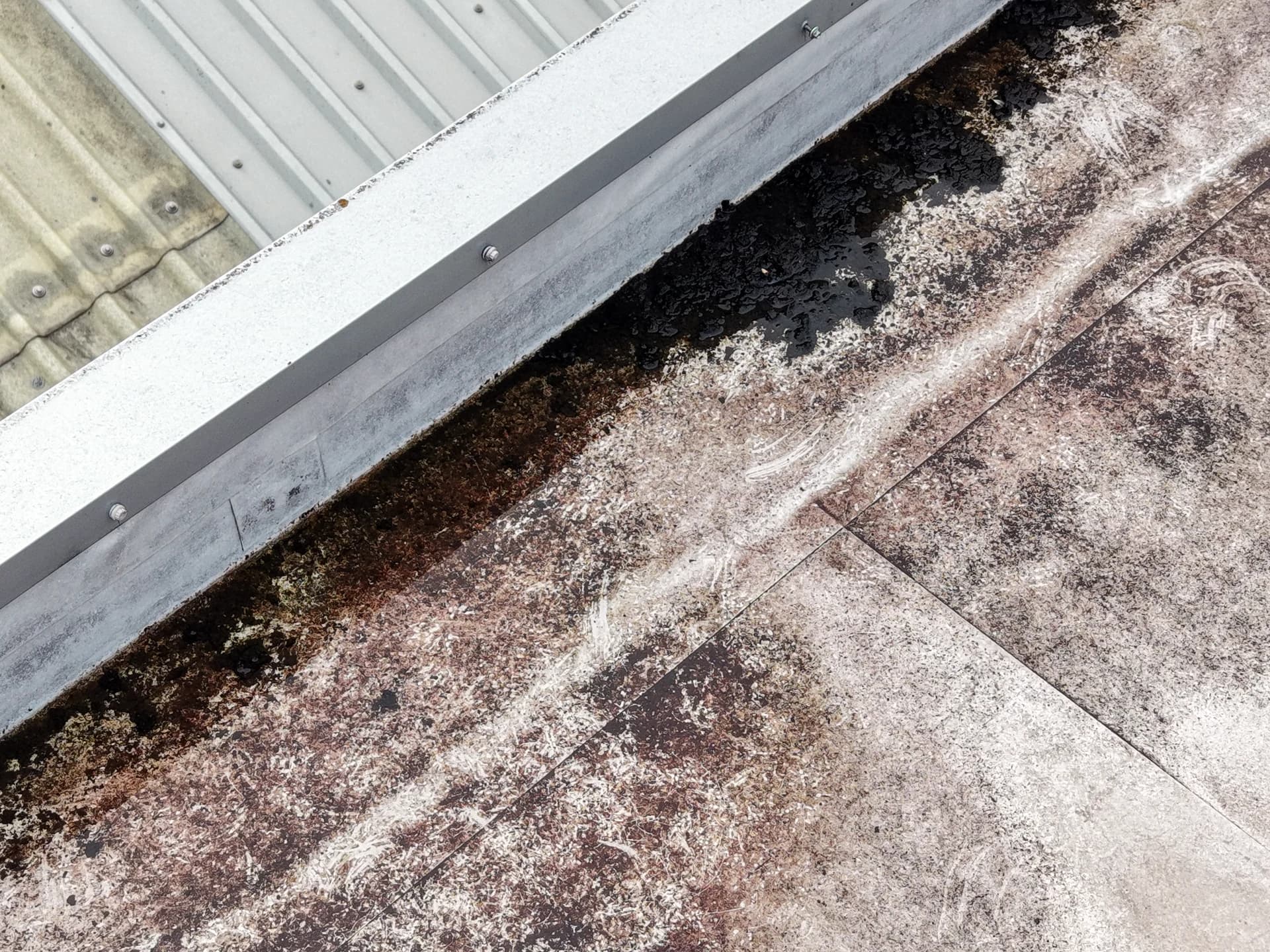 Aerial view of a parapet box gutter with a stained membrane beside a profiled-metal roof