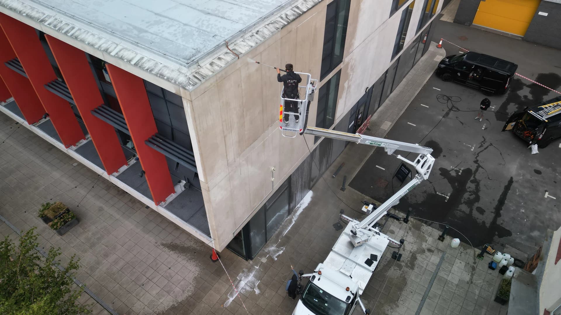 Aerial view of a technician in the basket of a truck-mounted access platform jetting a concrete panel elevation, coned off below