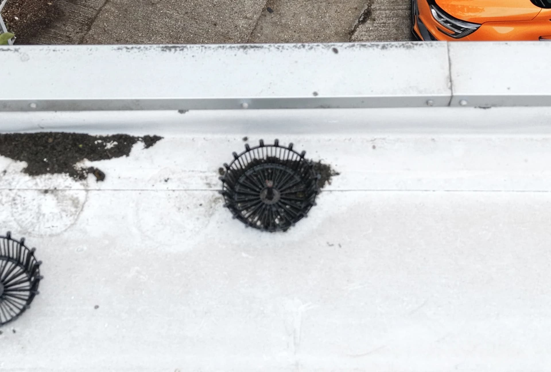 Aerial view of black leaf-guard domes over roof outlets with debris collected on a white membrane