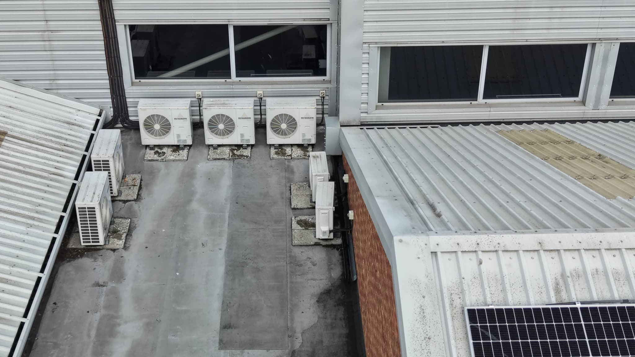 Aerial view of profiled metal cladding and windows above a flat section with outdoor air-conditioning plant