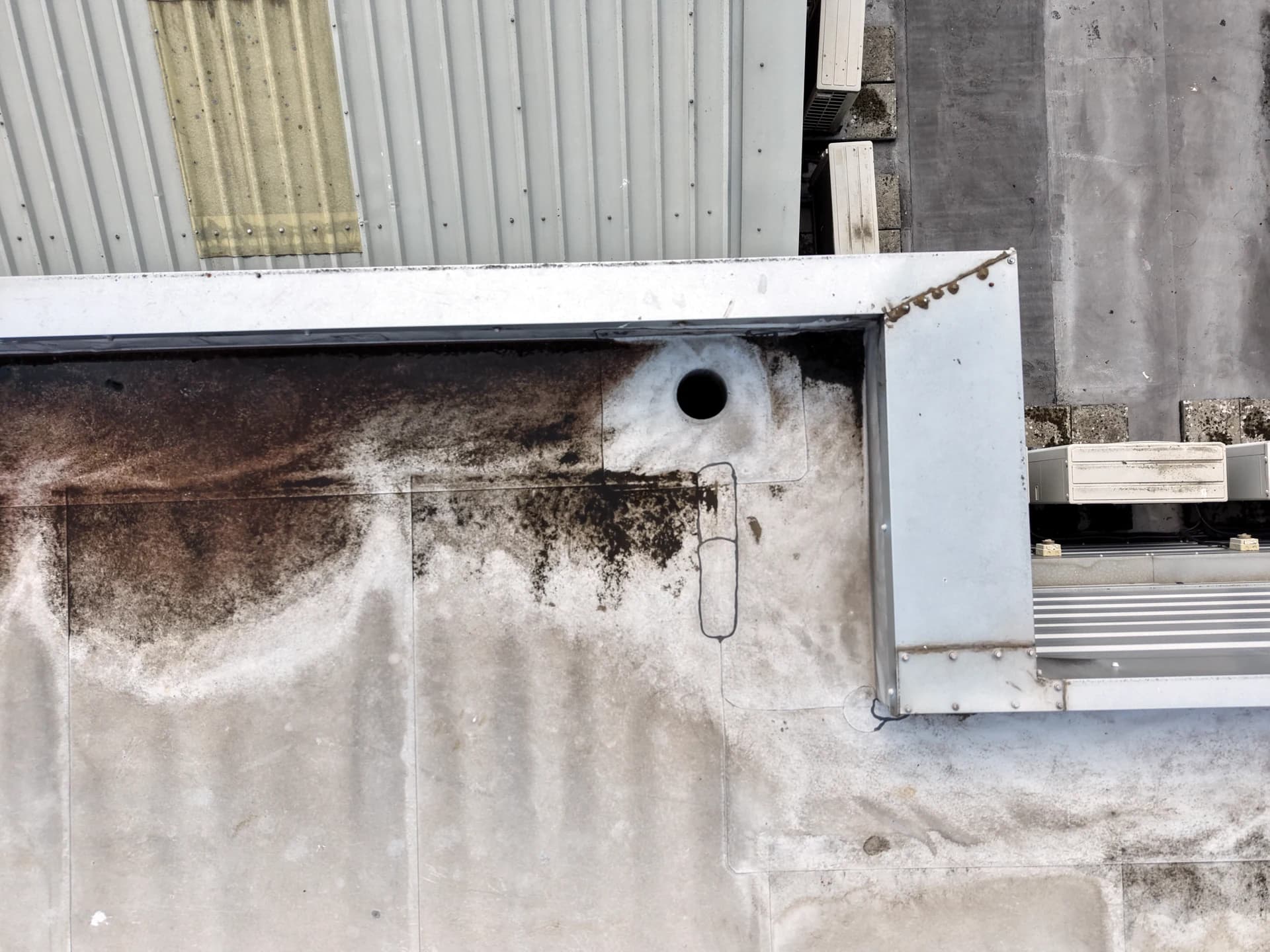 Aerial view of scalloped algae and rust staining along the foot of a metal parapet on a flat roof
