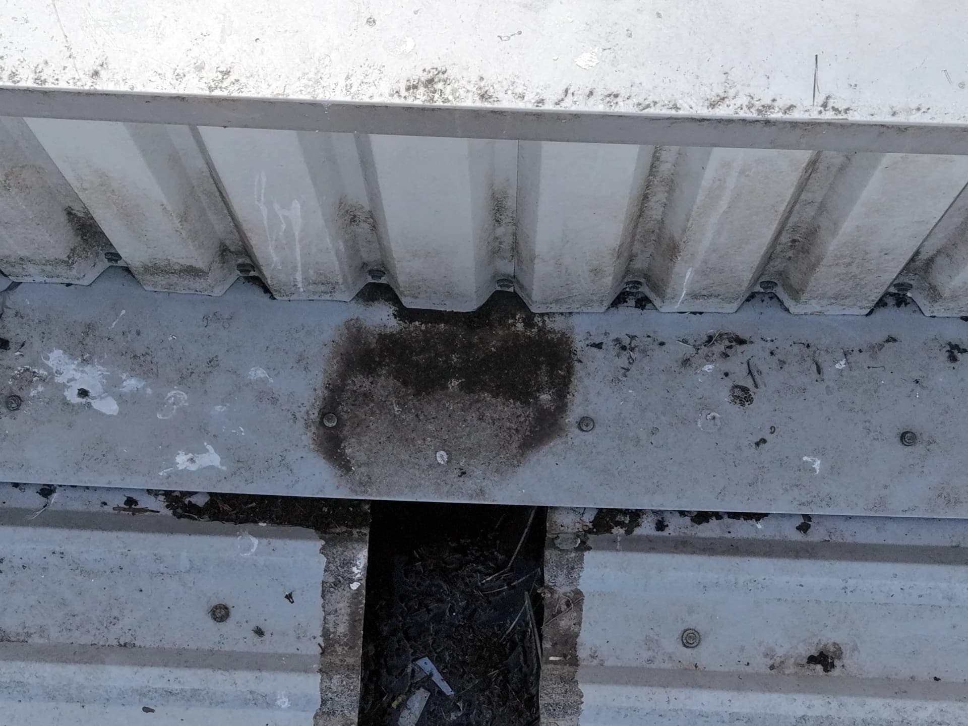 Close aerial view of a valley gutter outlet with a dark deposit on the flashing and debris in the channel