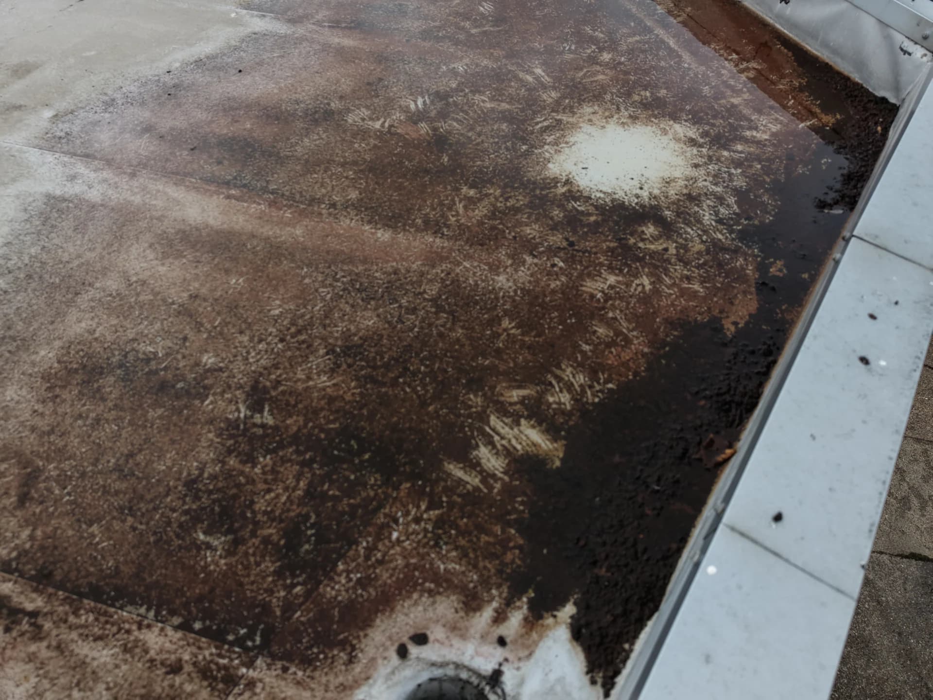 Close aerial view of heavily stained roof membrane around an outlet at the edge of a flat roof
