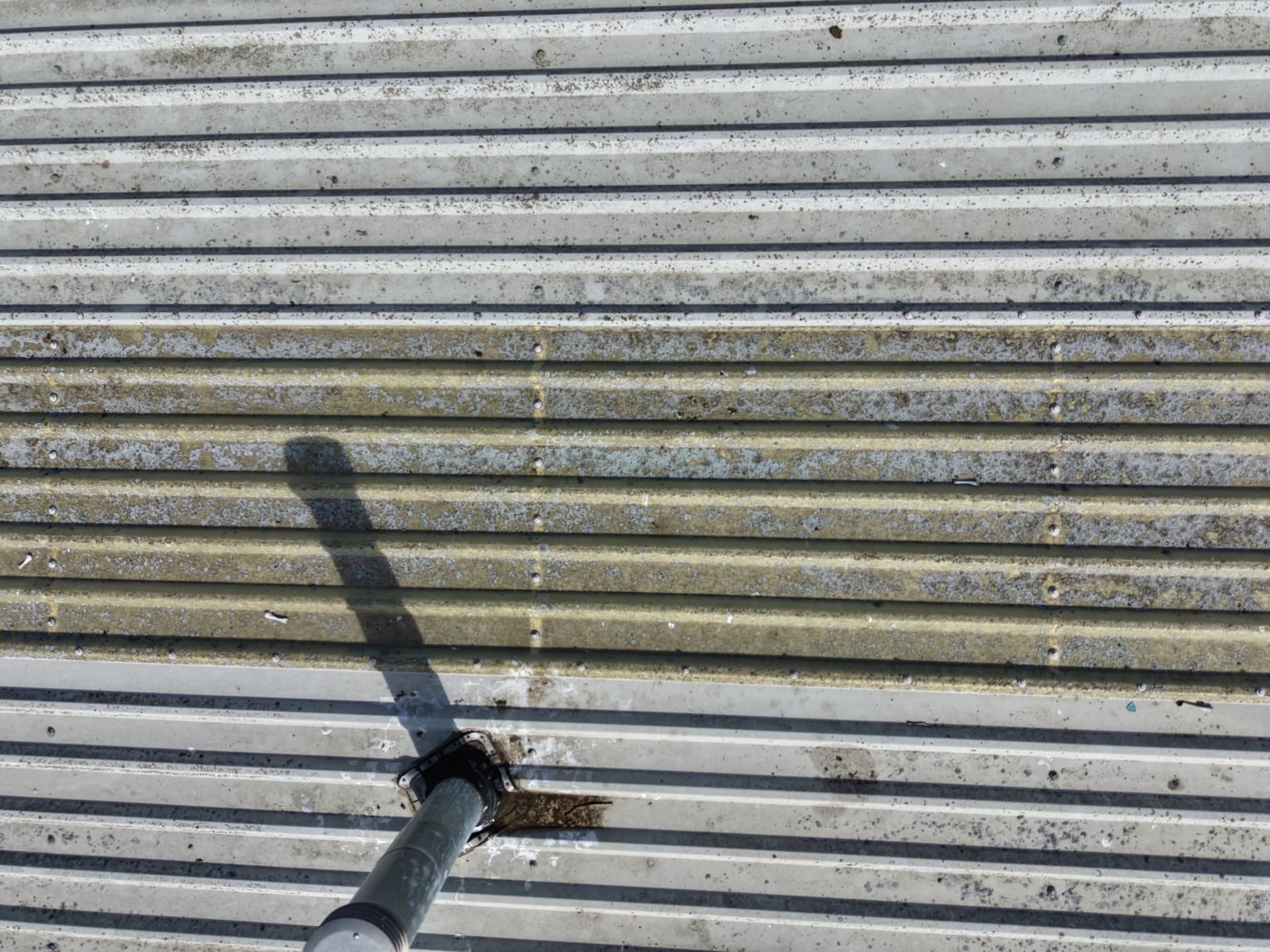 Close-up of a roof vent pipe on corrugated sheet with shadow.