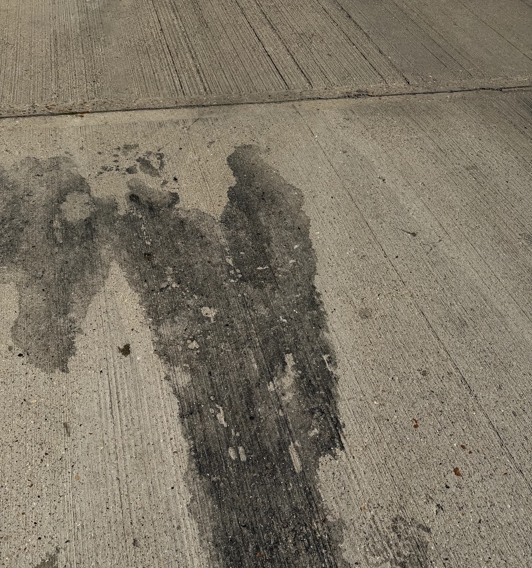 Close view of a long dark oil run on concrete hardstanding in clear light