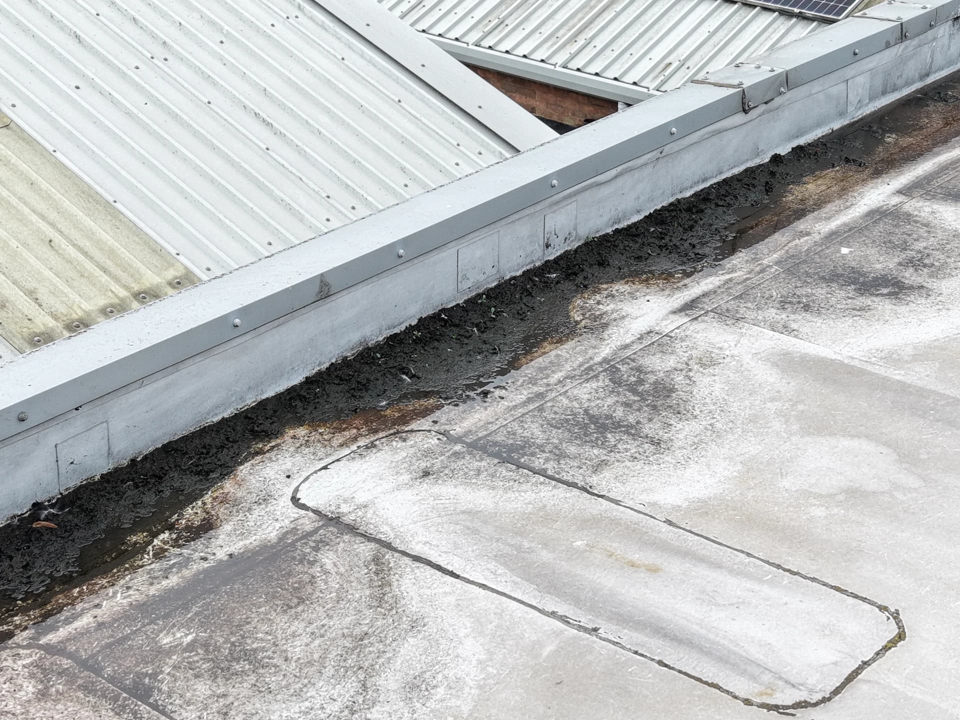 Debris and silt collected in a roof valley against a parapet upstand with a patched seam