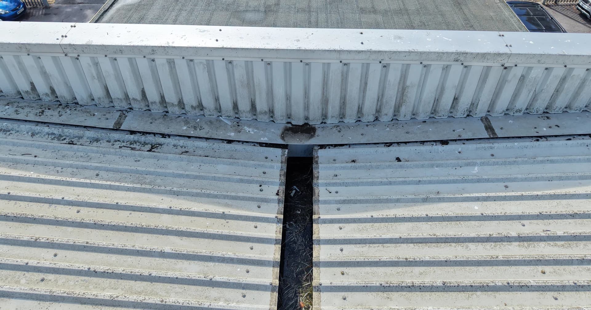 Oblique aerial view of a valley gutter with debris running into a parapet over a flat roof
