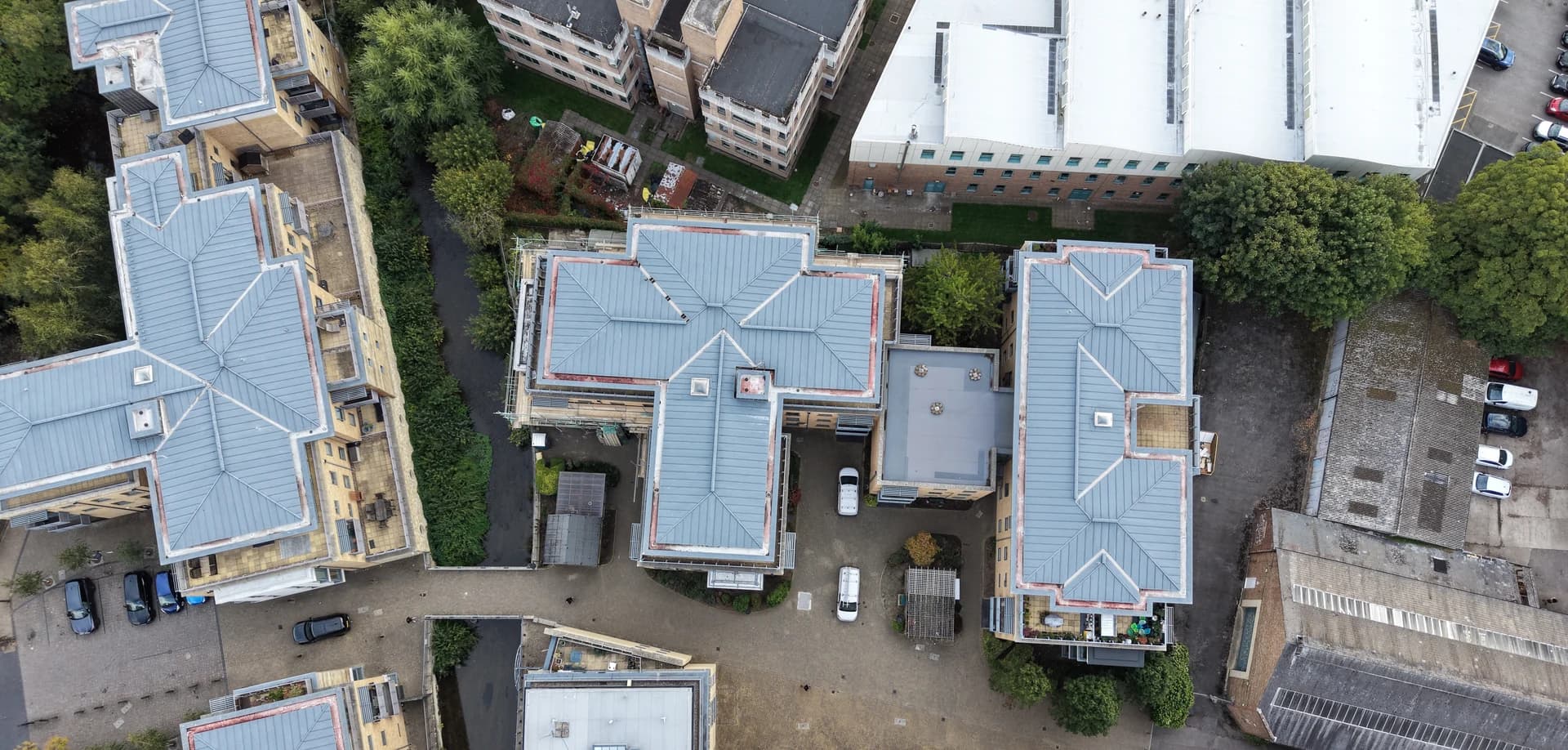 Overhead aerial view of three metal-roofed apartment blocks around a block-paved courtyard