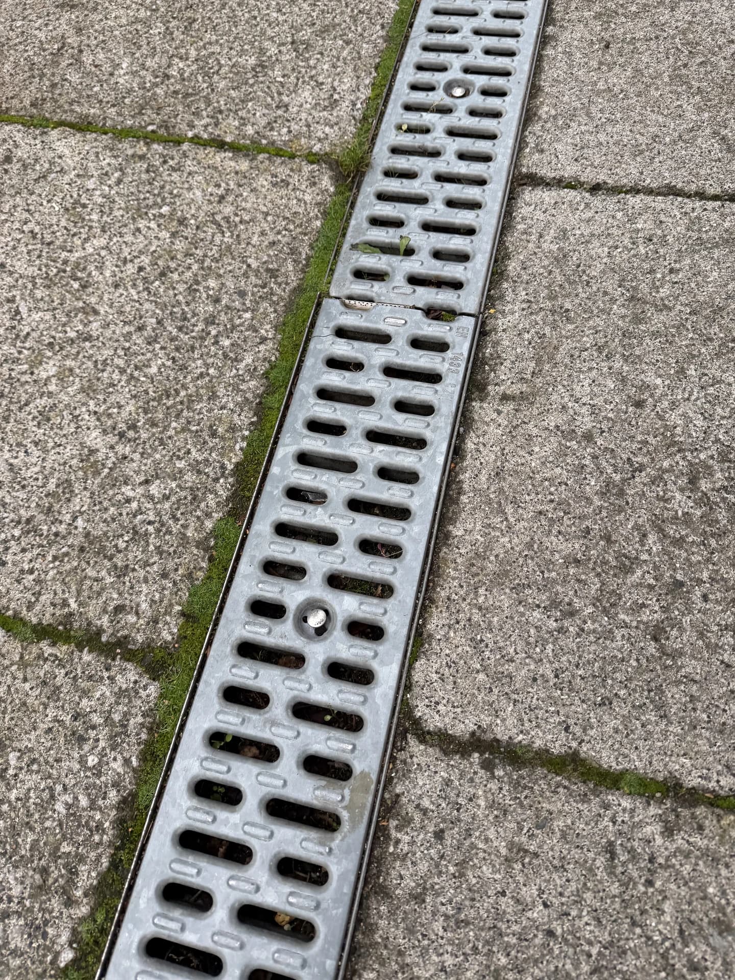 Overhead view of a galvanised drainage channel with moss growing along the paving edge