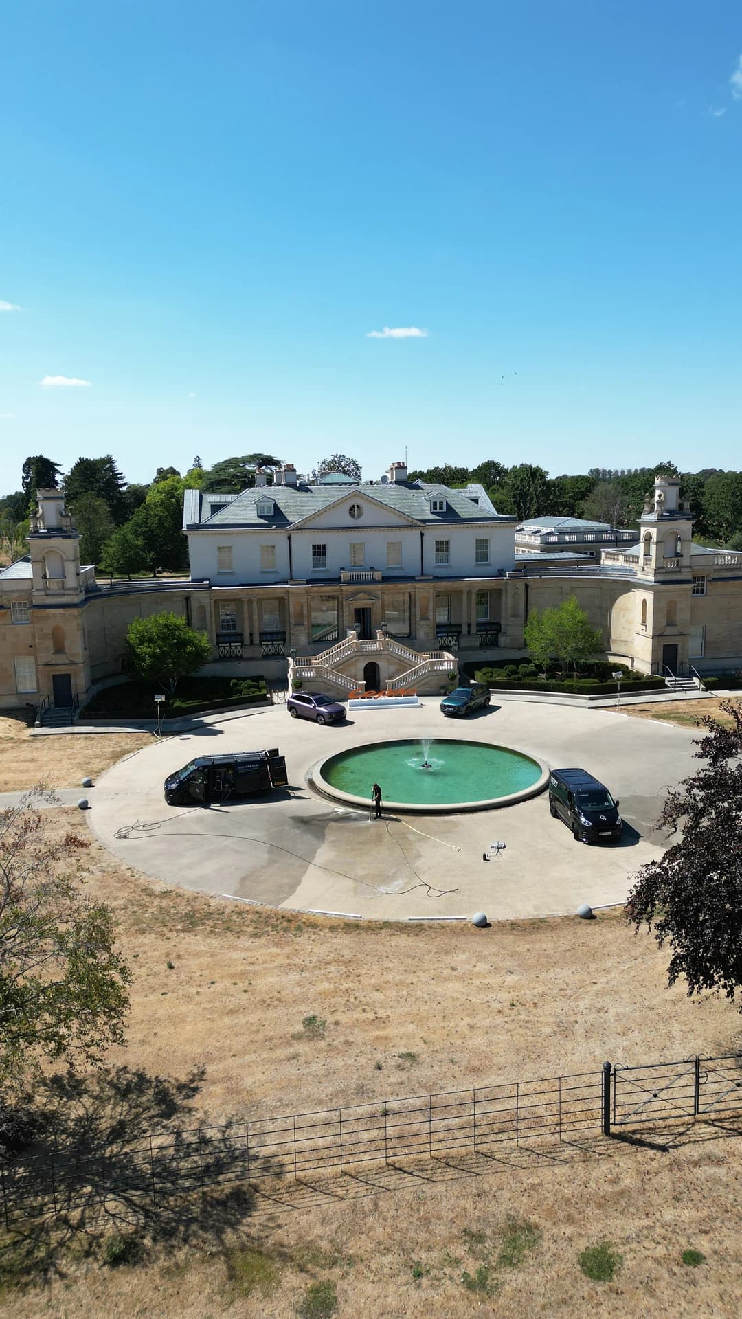 Portrait elevated wide of the forecourt with vans and the technician mid-clean, cleaned arc visible.