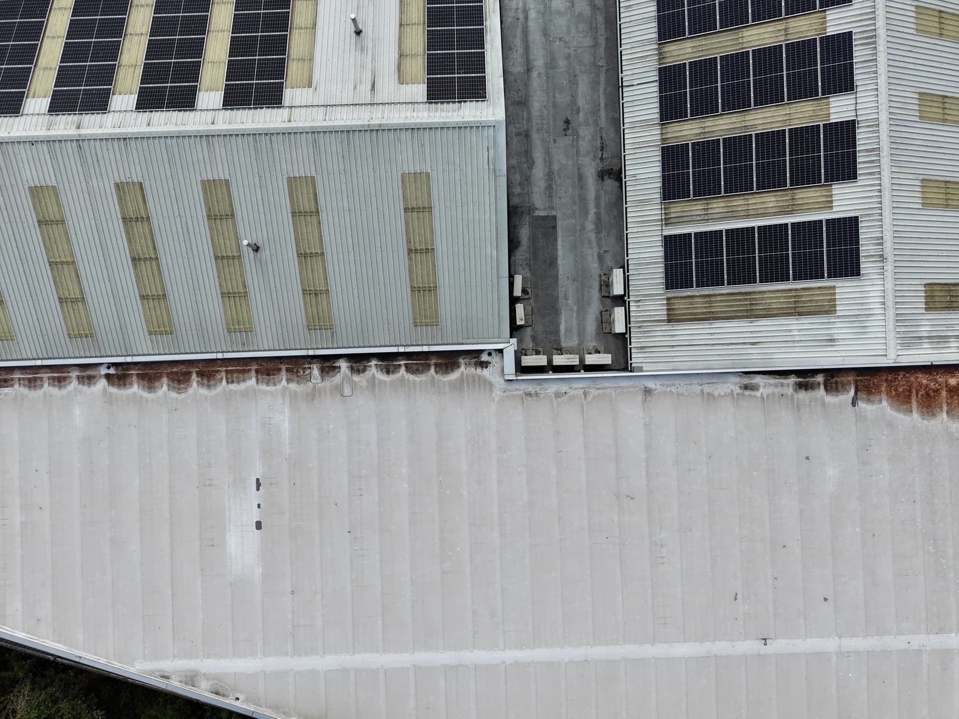 Roof edges and cladding junctions with rust-brown run-off staining; cars parked alongside.