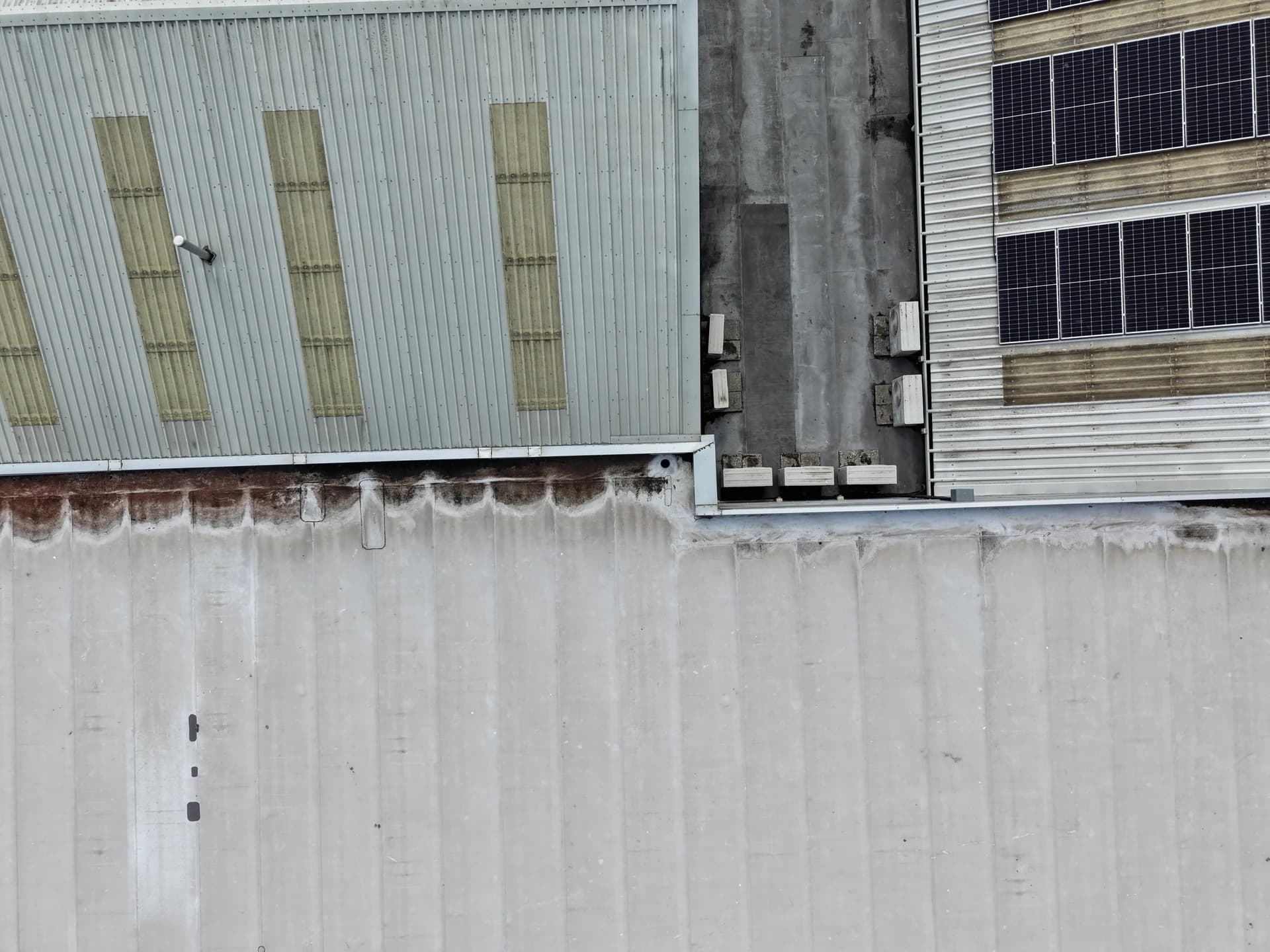 Roof edges and cladding junctions with rust-brown run-off staining; cars parked alongside.