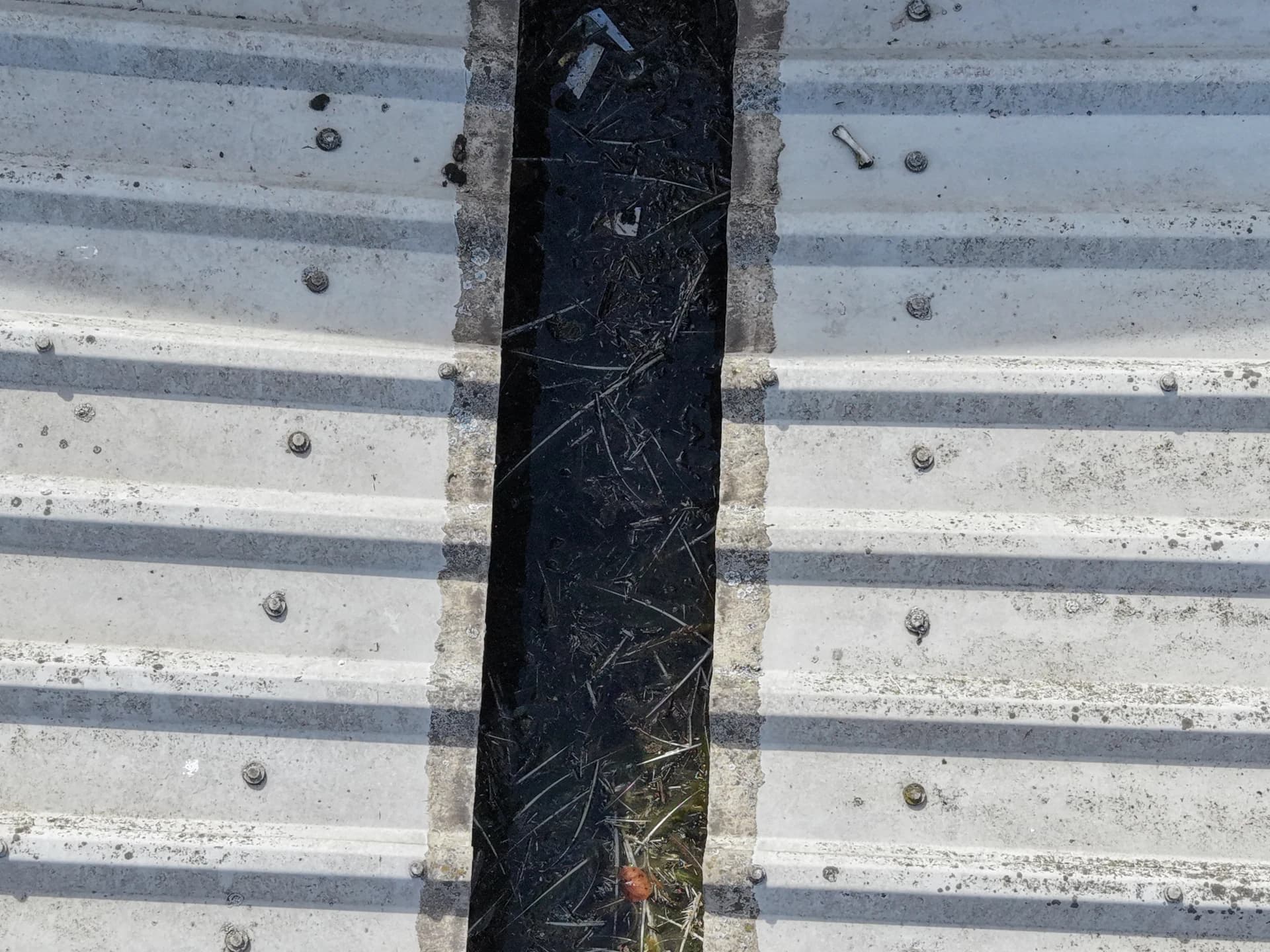 Top-down aerial view of a valley gutter with debris between corrugated roof sheets