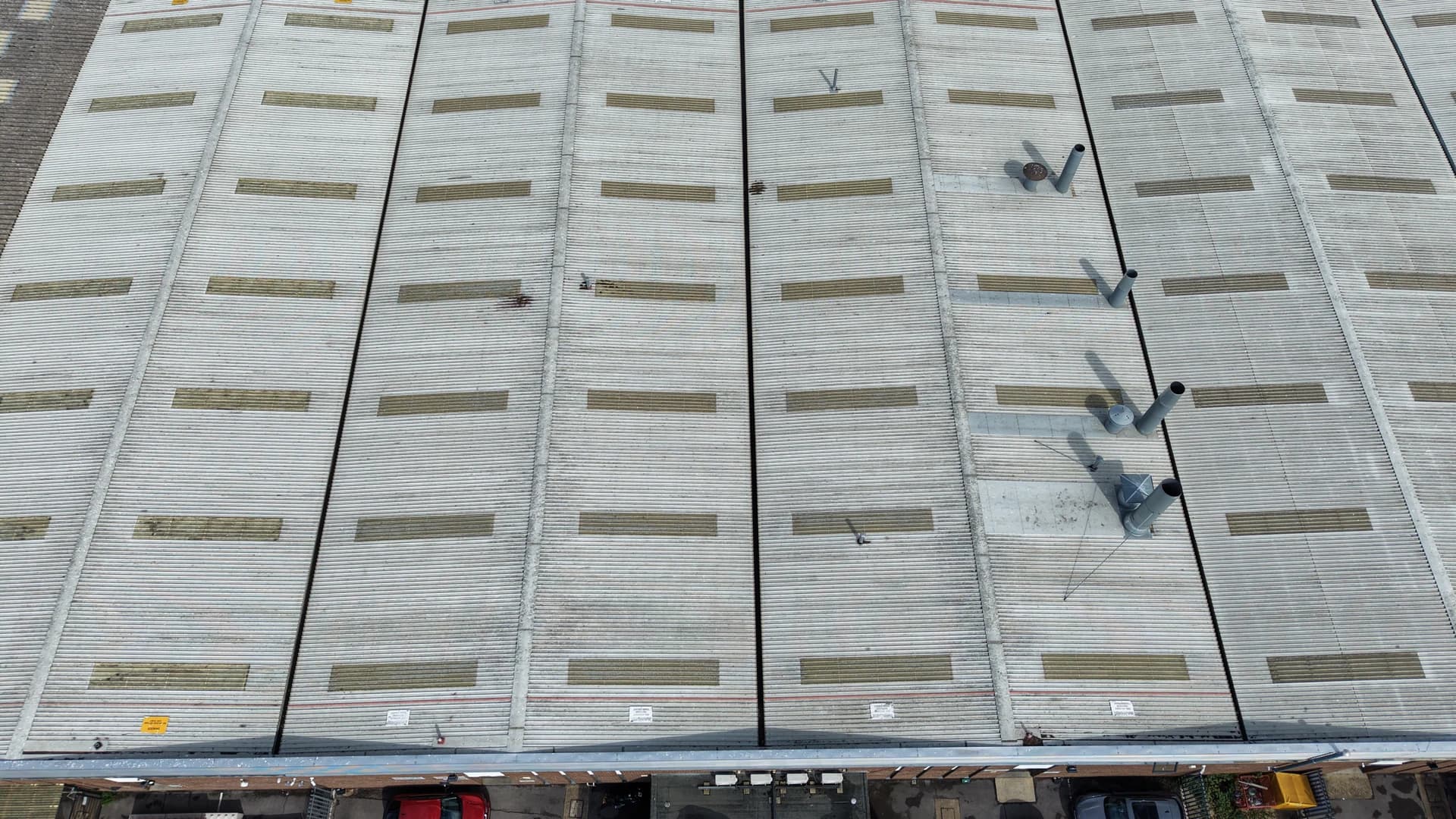 Top-down aerial view of a whole industrial roof with a yard and car park above and below it