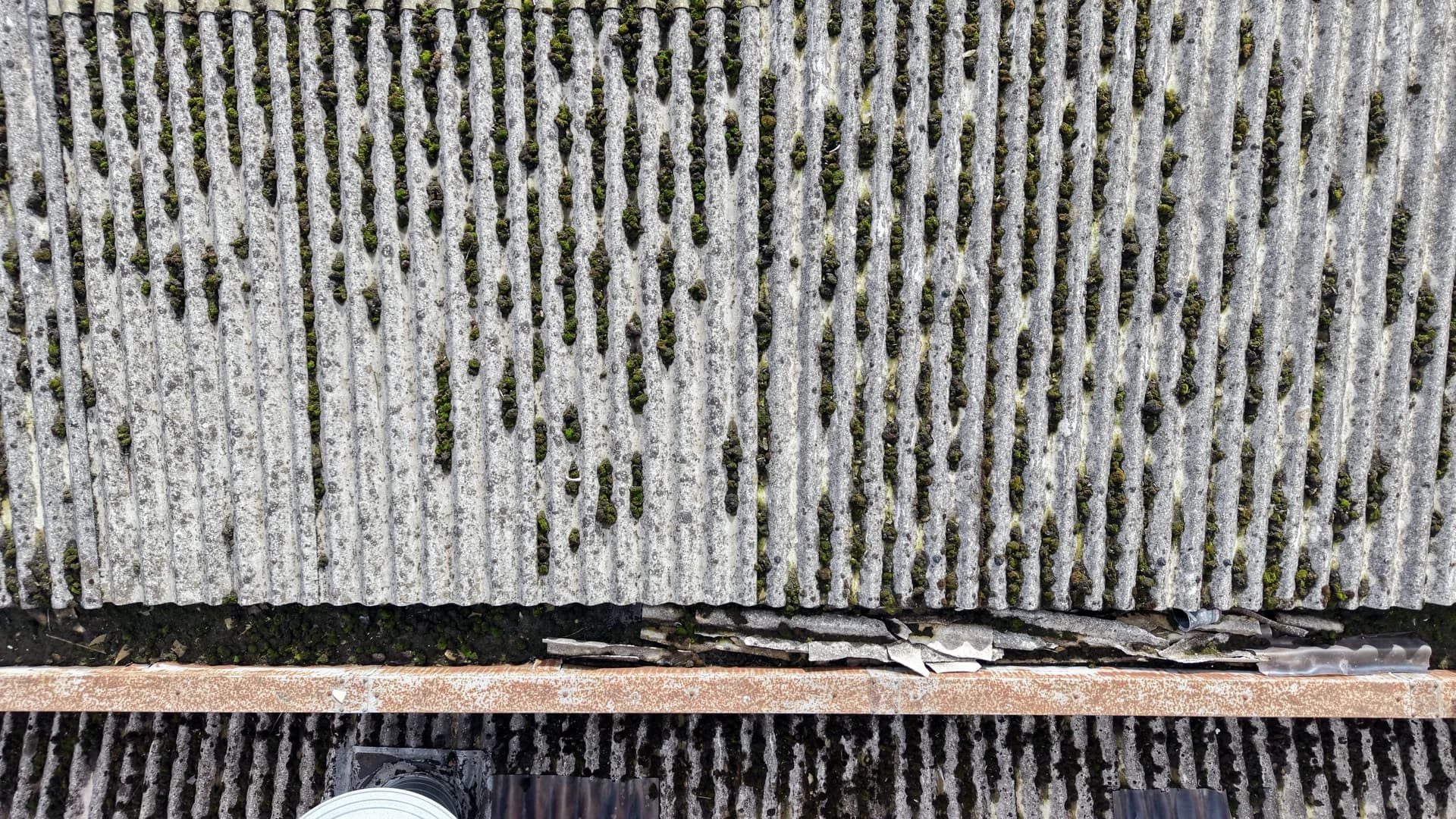 Top-down view of a roof edge at the gutter line with damaged sheet ends and a roof vent