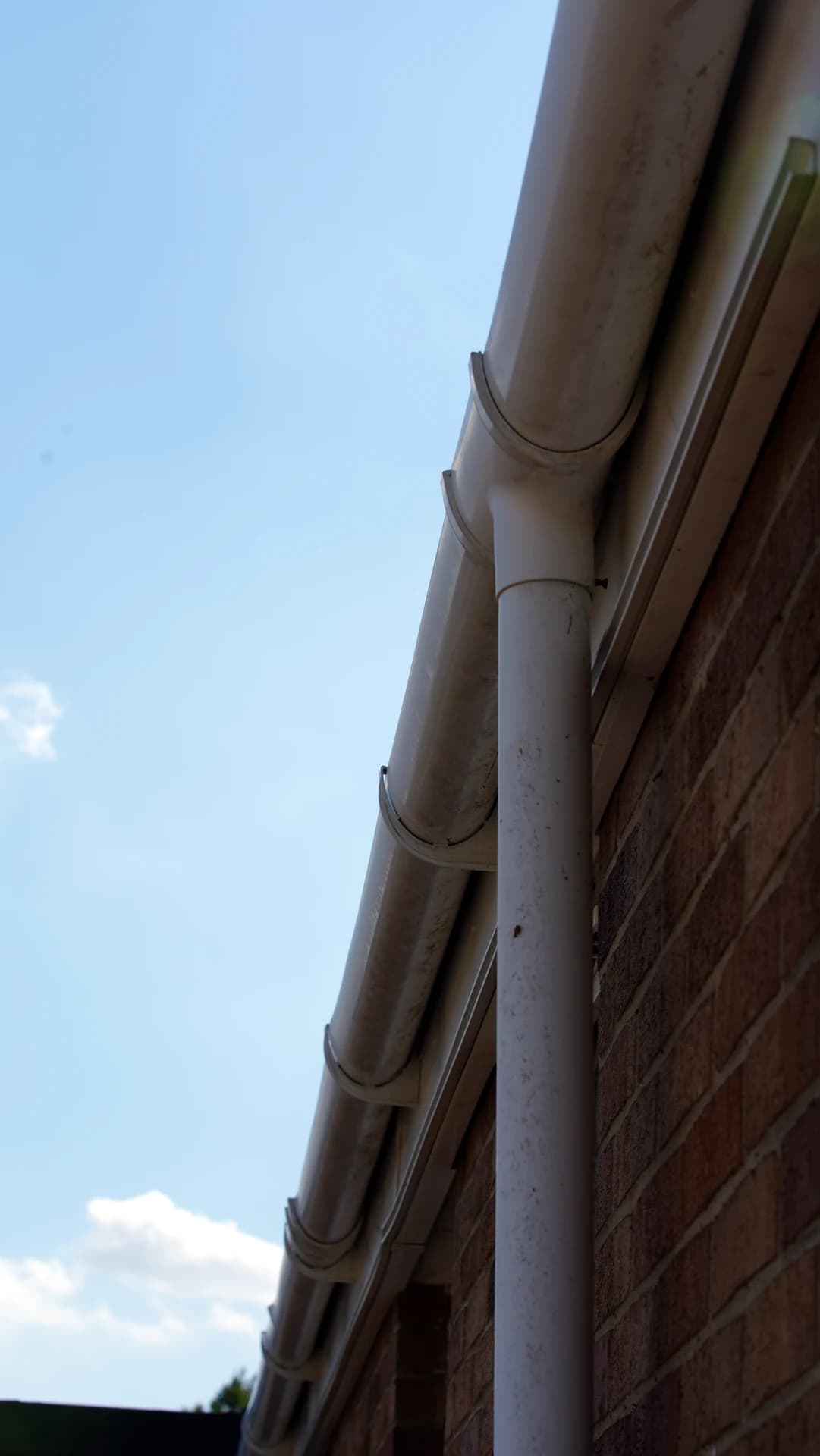 Upward view of a long gutter run with downpipe on a brick wall, lightly weathered.