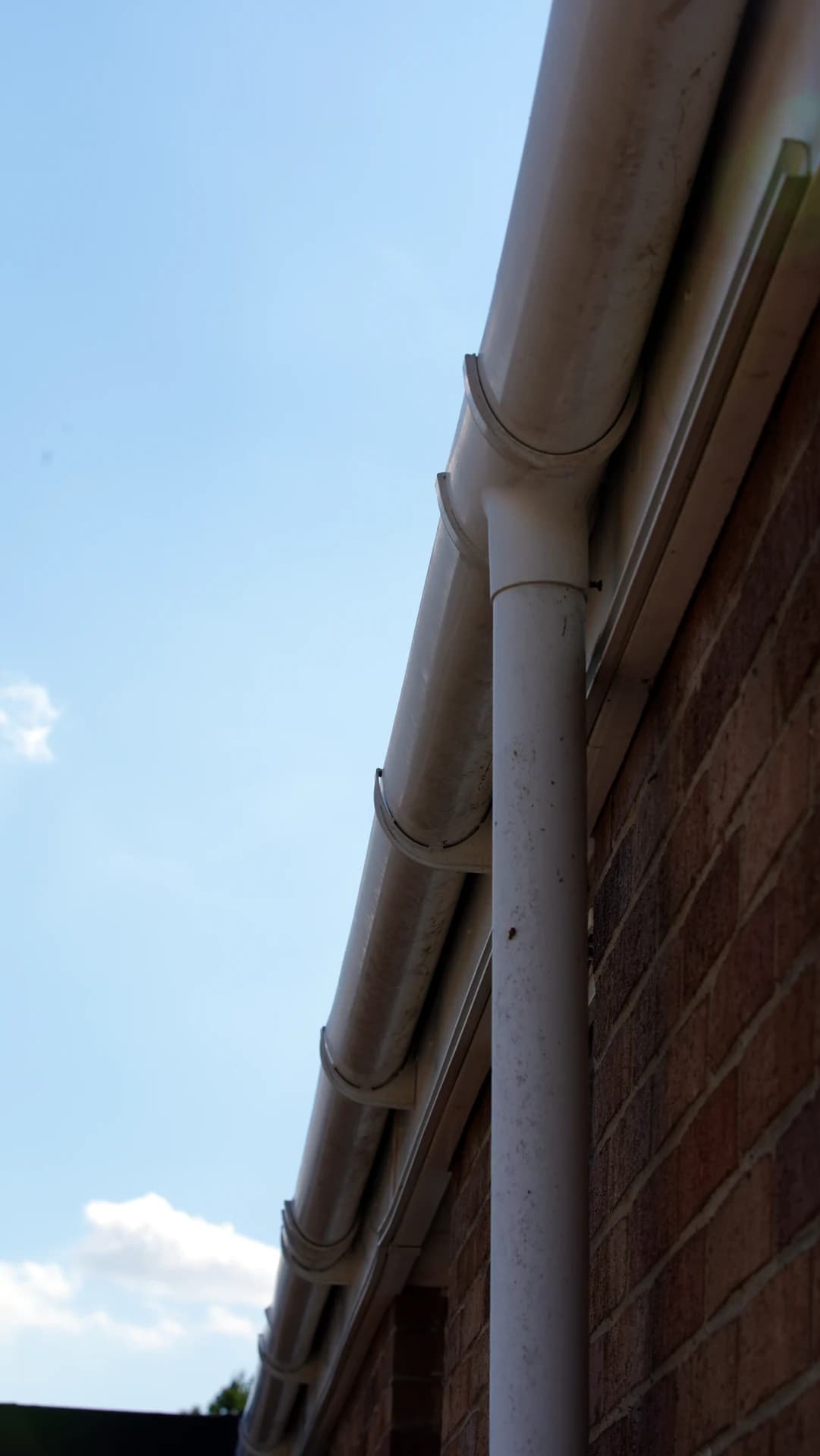 Upward view of a long gutter run with downpipe on a brick wall, lightly weathered.
