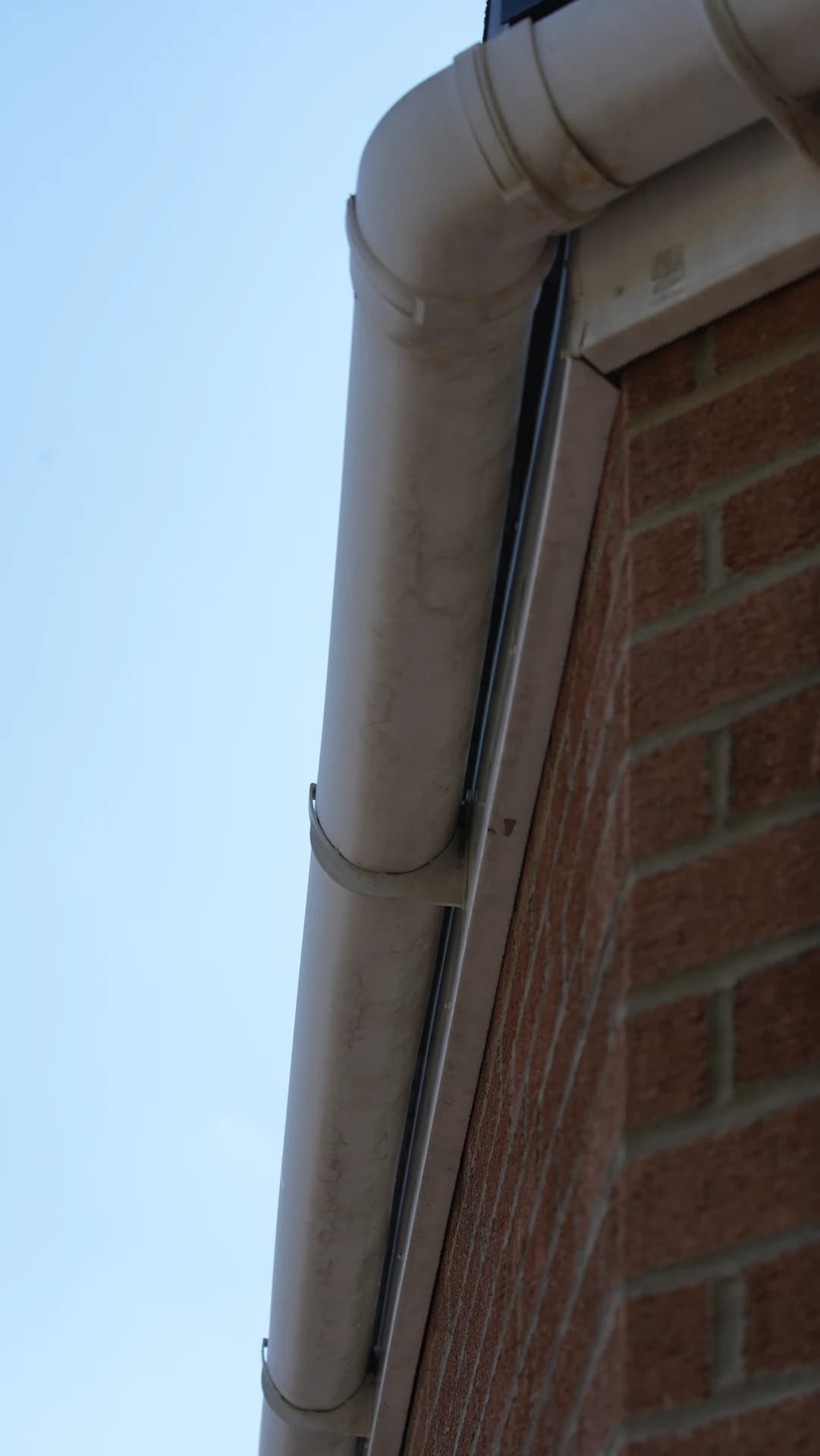Upward view of a stained half-round gutter end/corner and bracket against a brick gable.