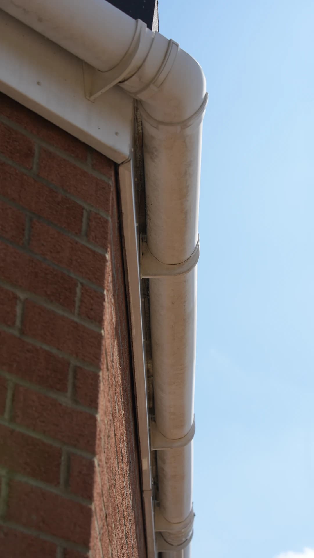 Upward view of a stained half-round gutter end/corner and bracket against a brick gable.
