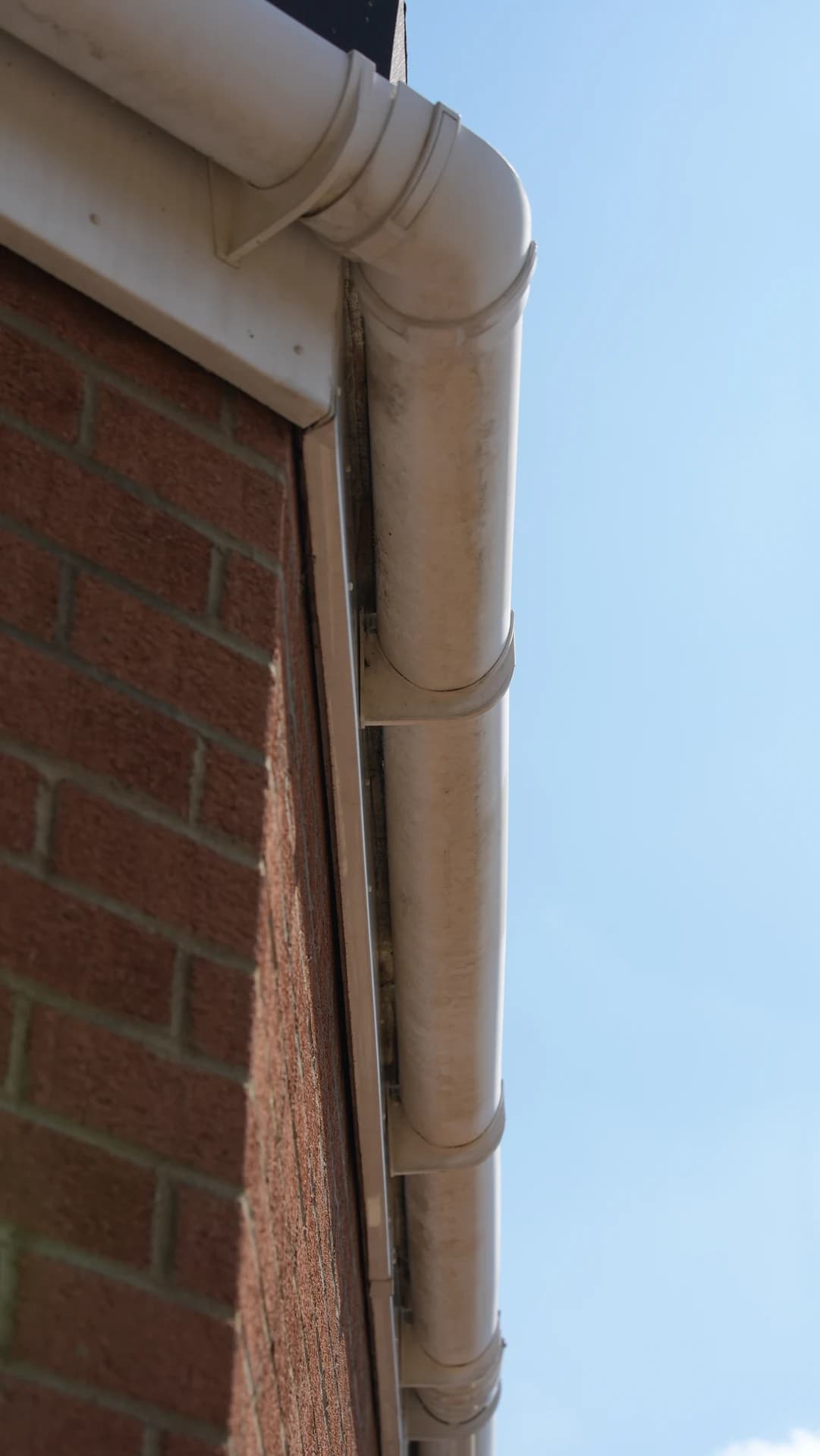Upward view of a stained half-round gutter end/corner and bracket against a brick gable.
