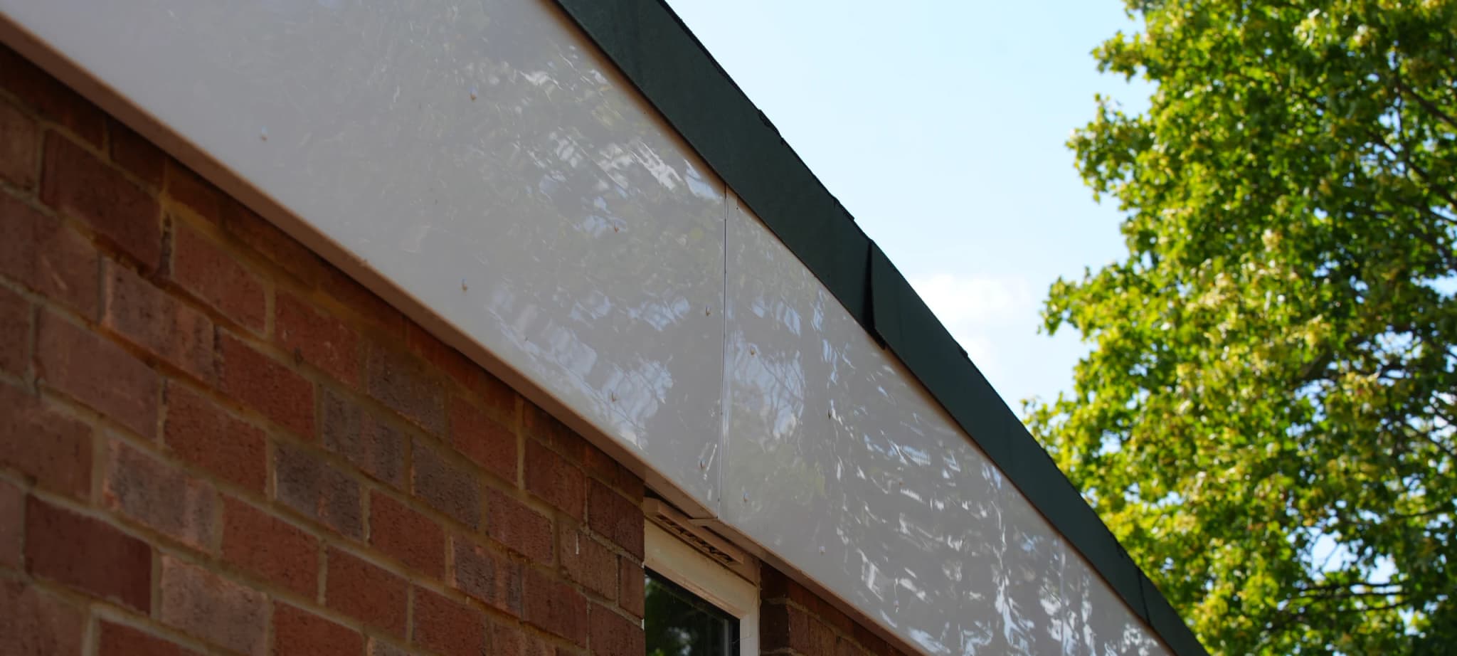Upward view along a white fascia panel above a brick elevation, the panel streaked with atmospheric staining